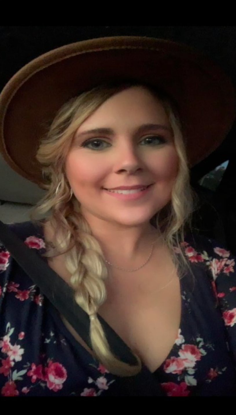 A woman wearing a hat and a floral dress is smiling.