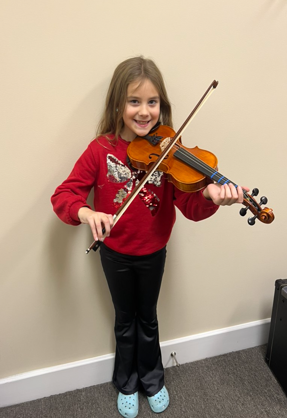 A young girl is playing a violin in a room.