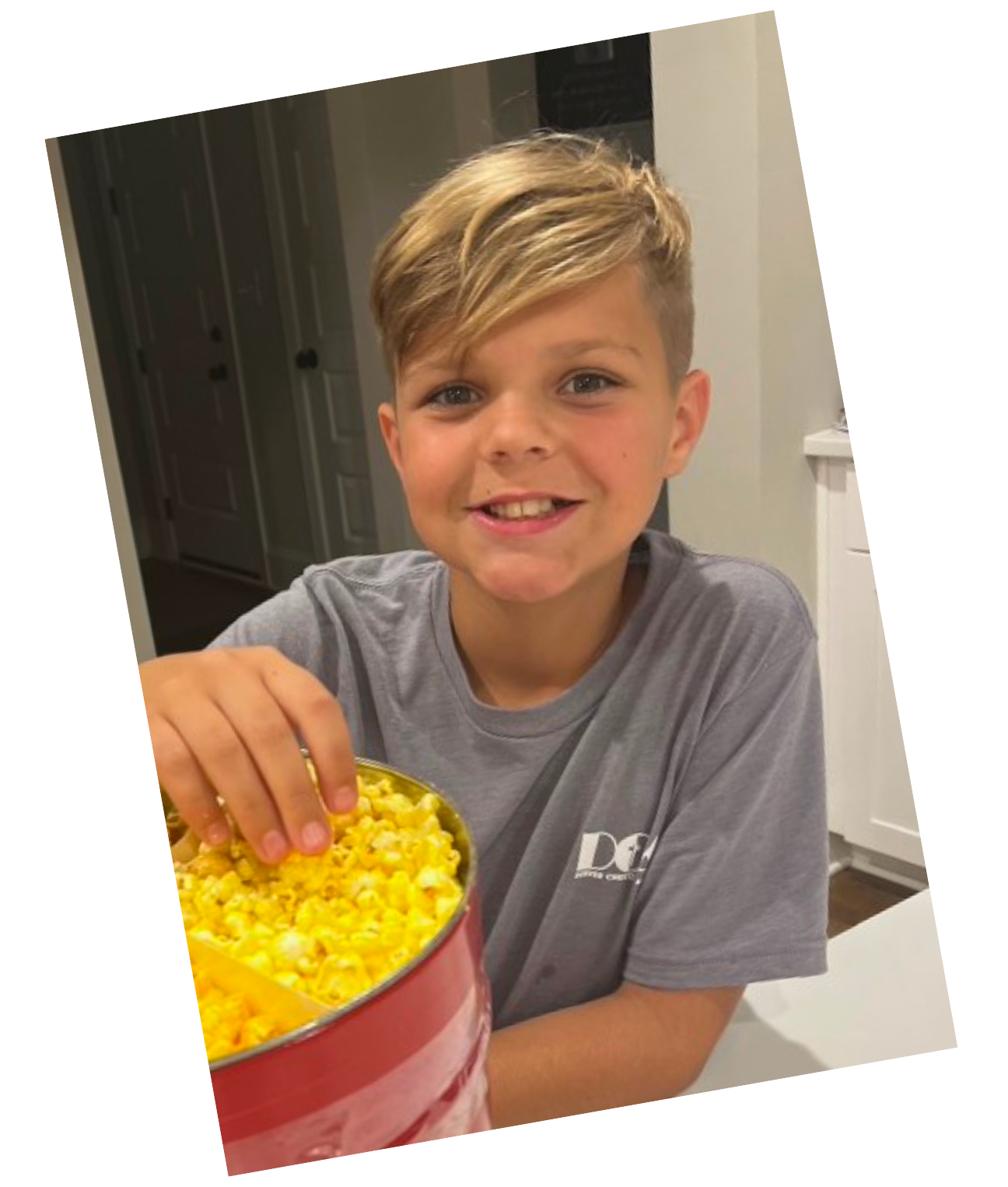 A young boy in a grey shirt is holding a tin of popcorn