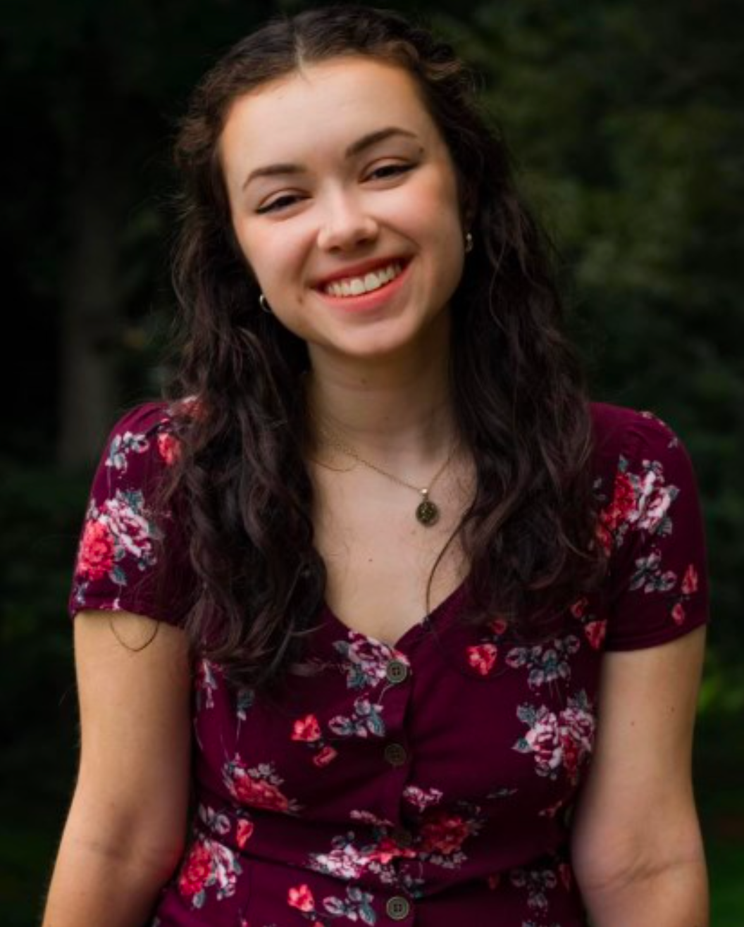 A woman in a purple floral dress is smiling for the camera
