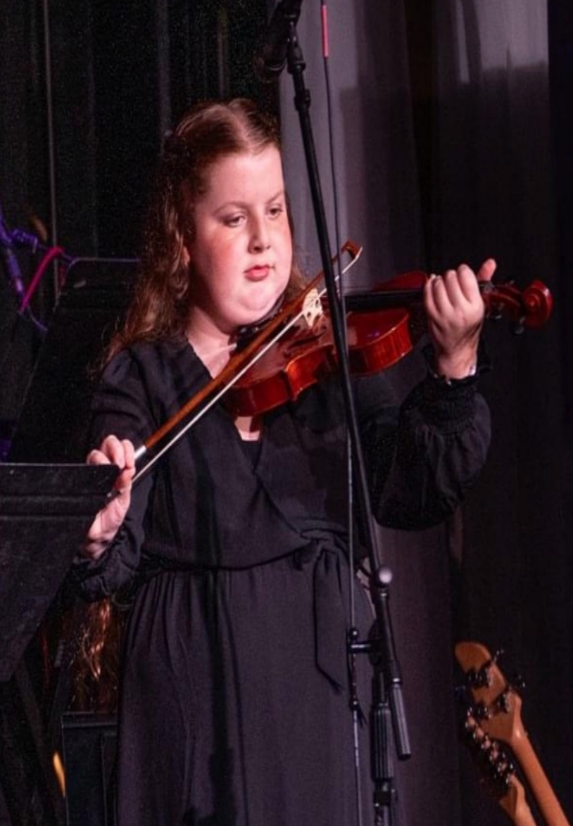 A young girl is playing a violin in a room.