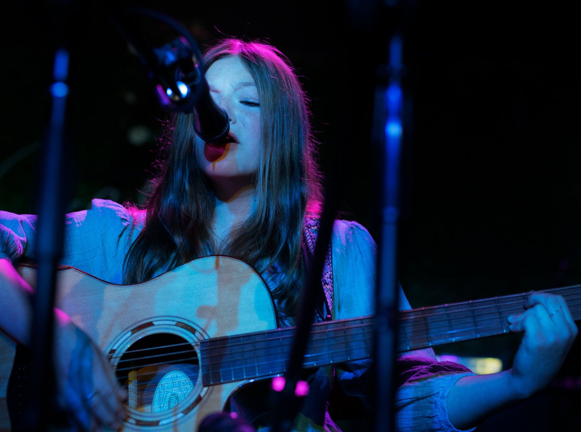 A girl is singing into a microphone while playing a guitar.