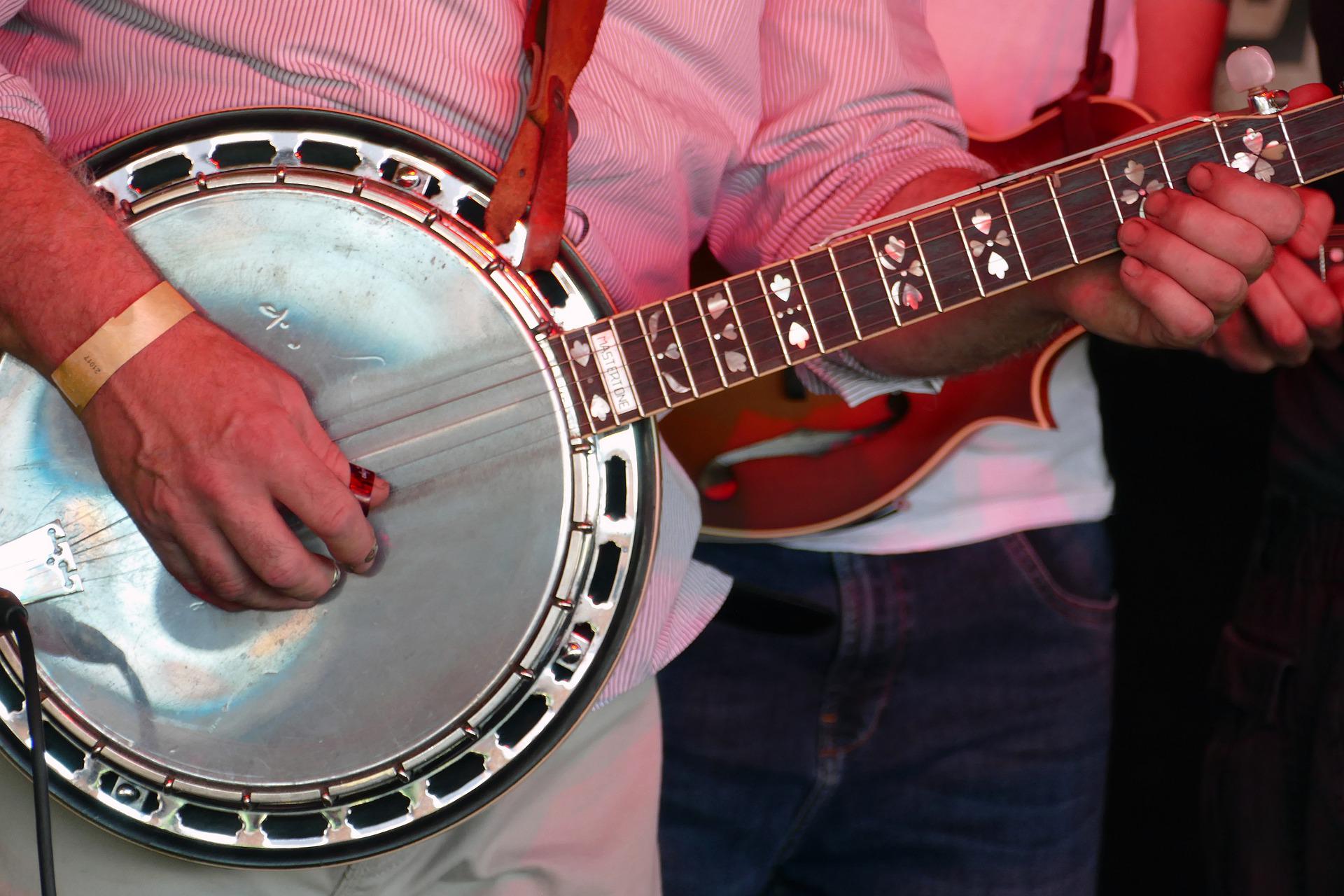 A man is playing a banjo with a guitar in the background