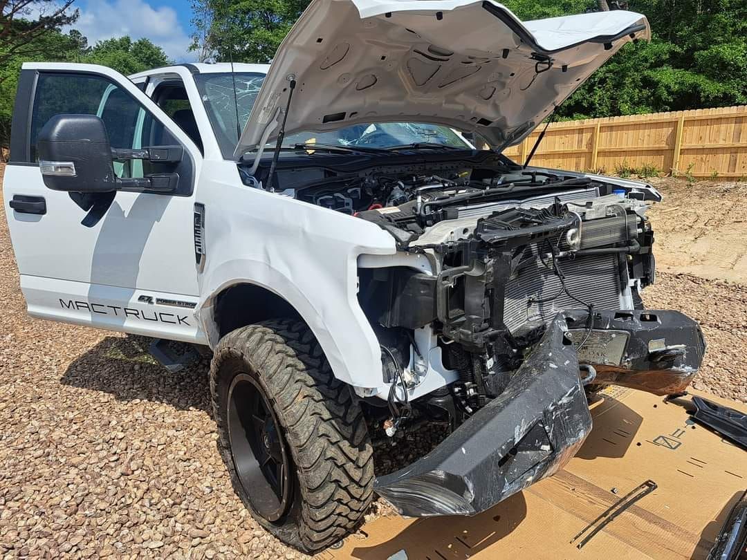A white truck with the hood up is sitting on top of a pile of gravel.