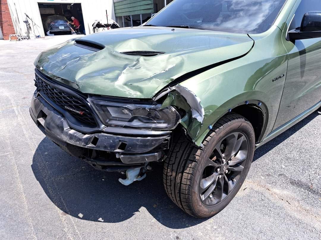 A green dodge ram with a damaged front end is parked in a parking lot.