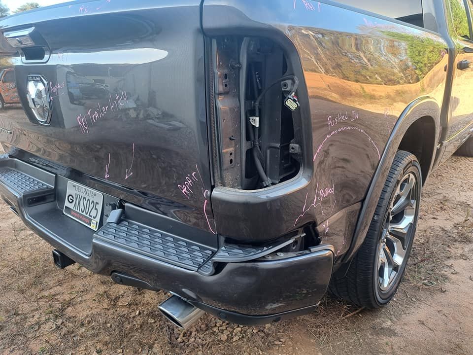 A ram truck with a damaged tailgate is parked in the dirt.