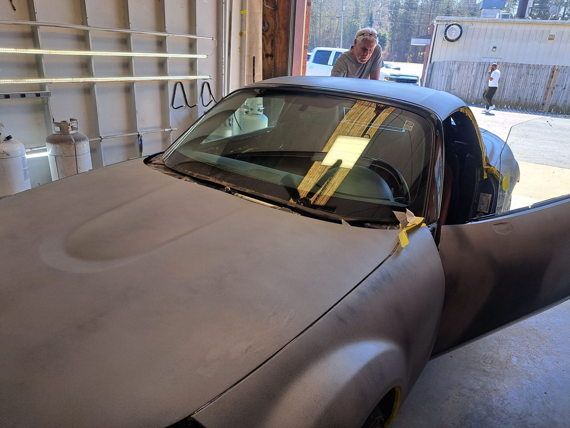 A man is standing next to a dirty car in a garage.