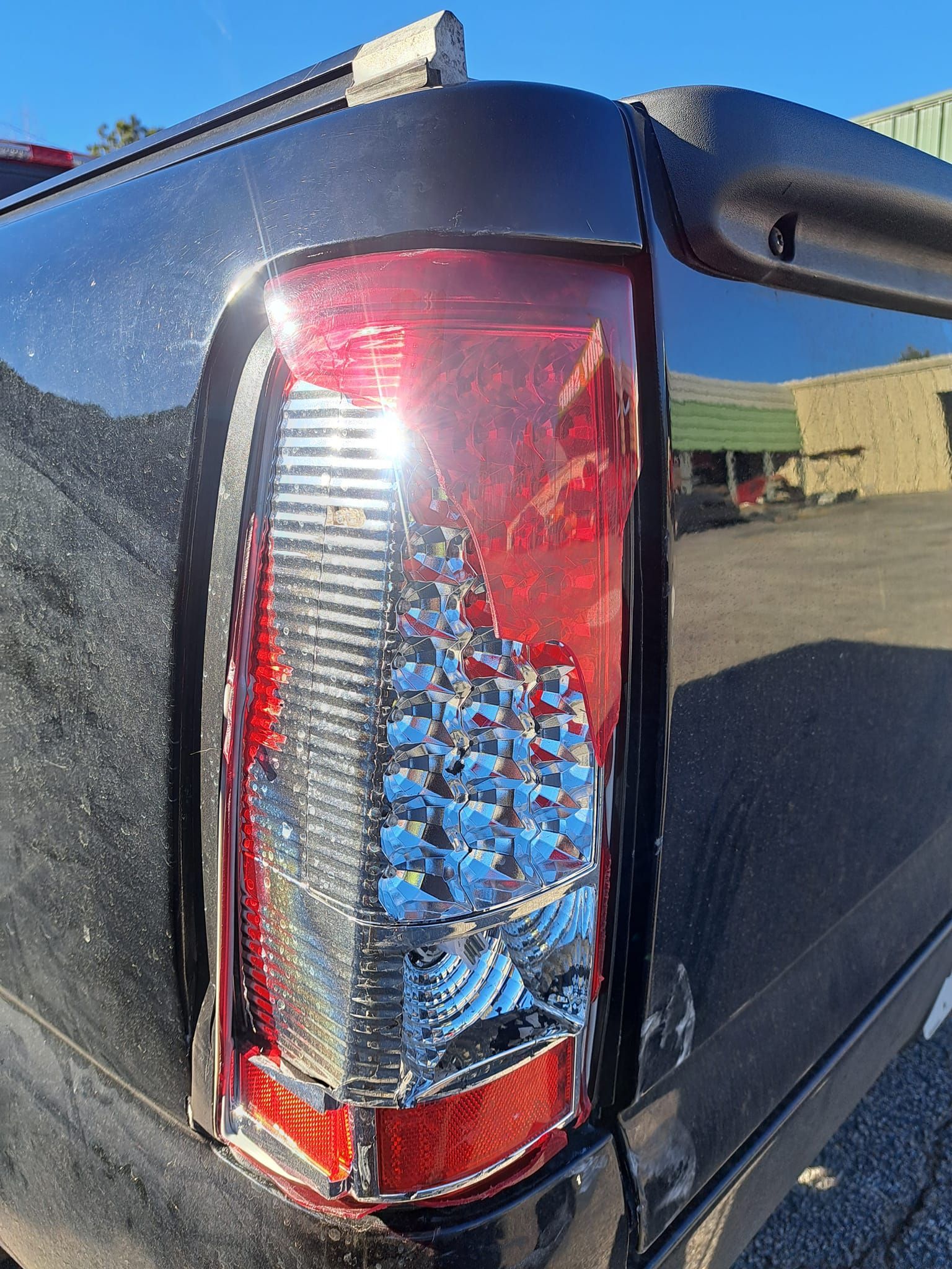 A close up of a black truck 's tail light in a parking lot.