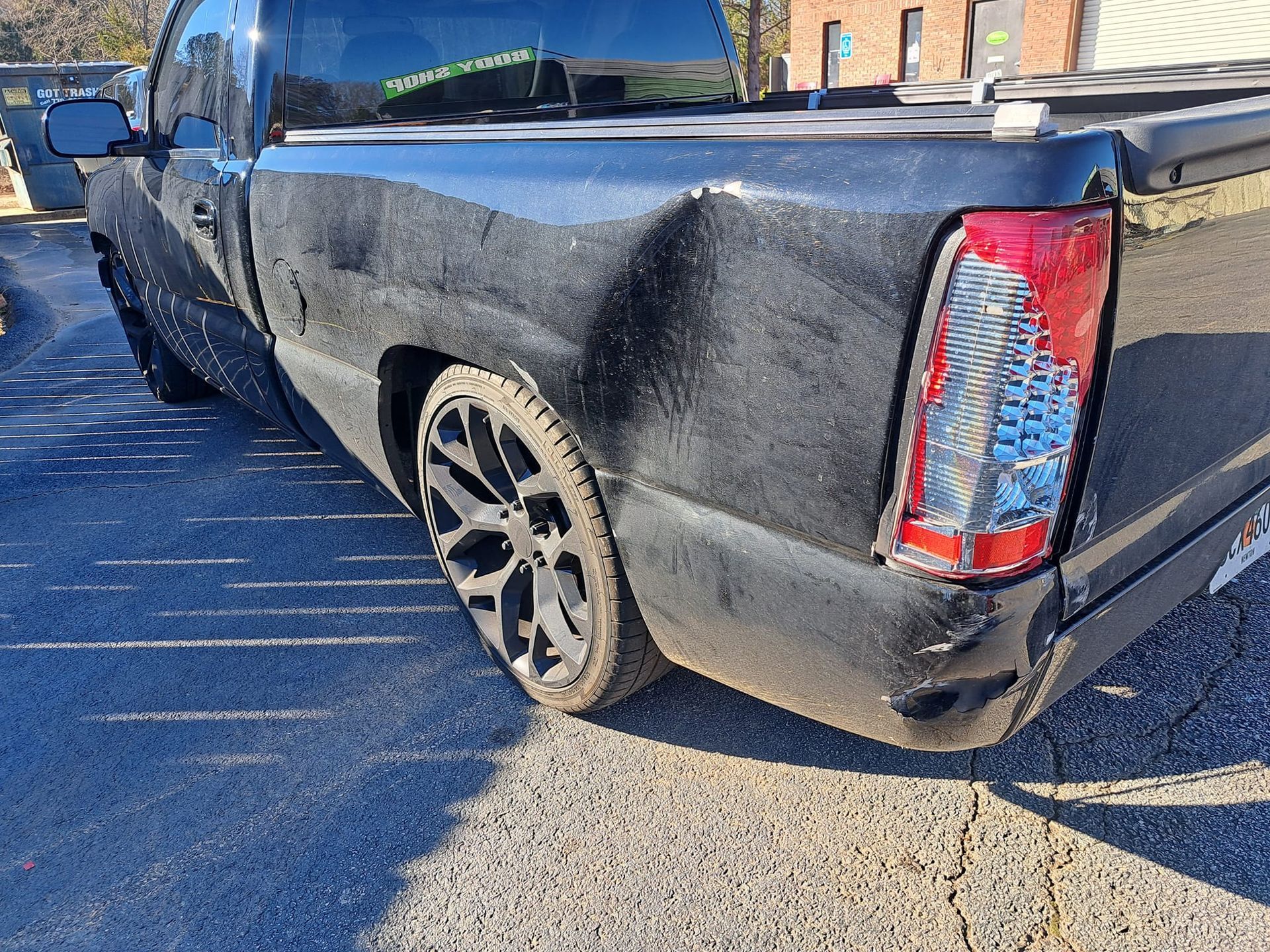 A black truck with a damaged bumper is parked in a parking lot.