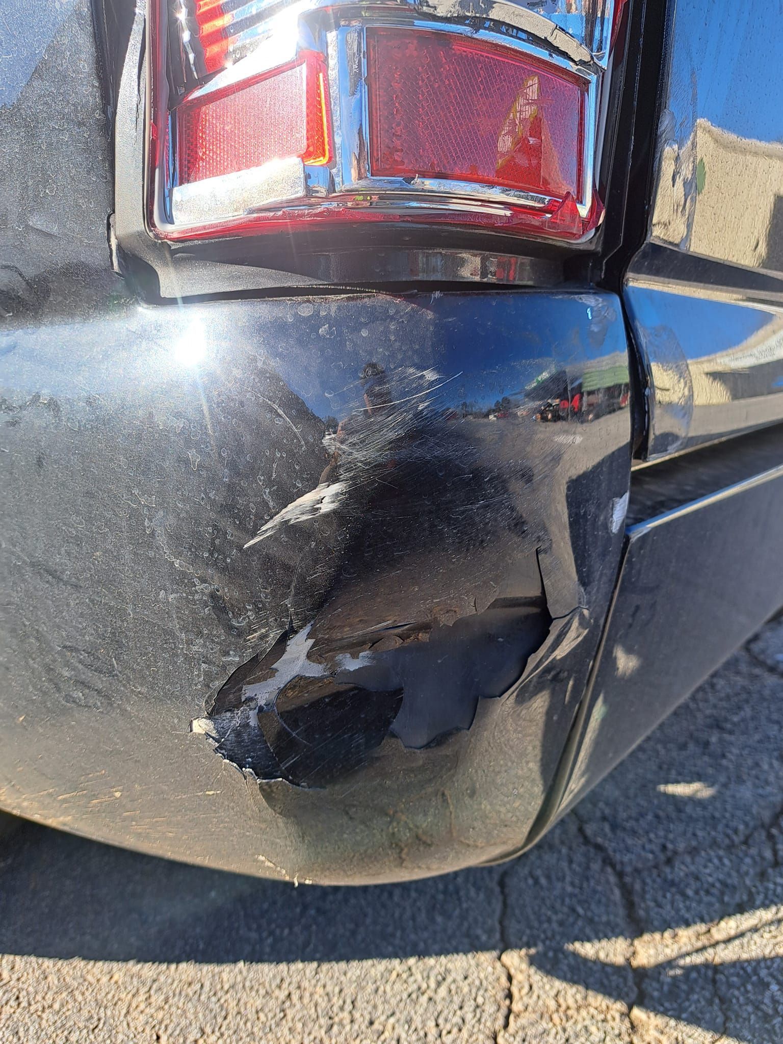 A close up of a black car with a damaged bumper and tail light.