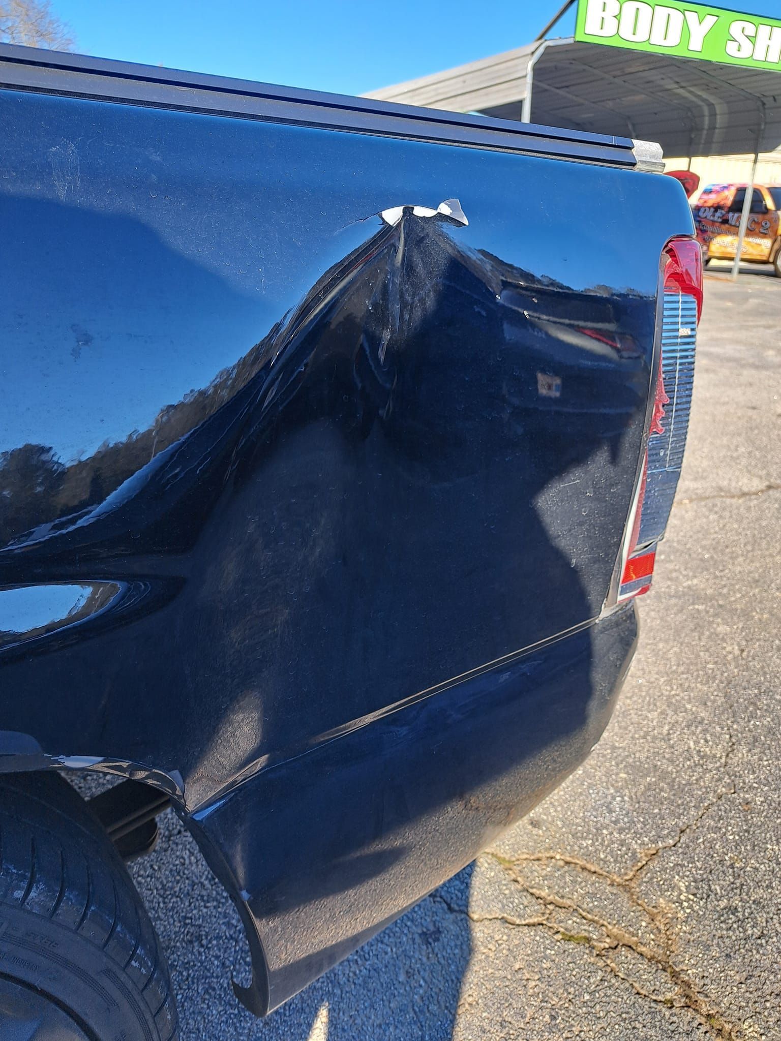 A black truck with a damaged tailgate is parked in front of a hobby shop.