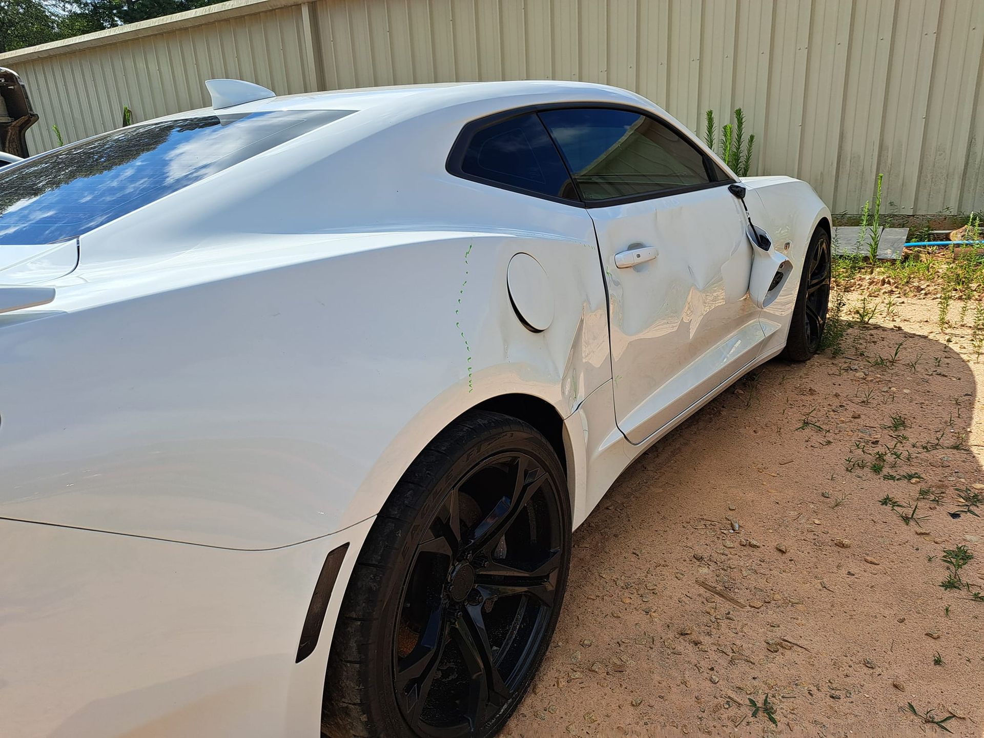 A white sports car with black wheels is parked in the dirt.