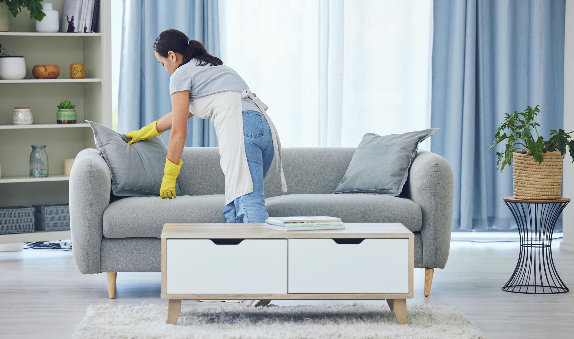 A woman is cleaning a couch in a living room.