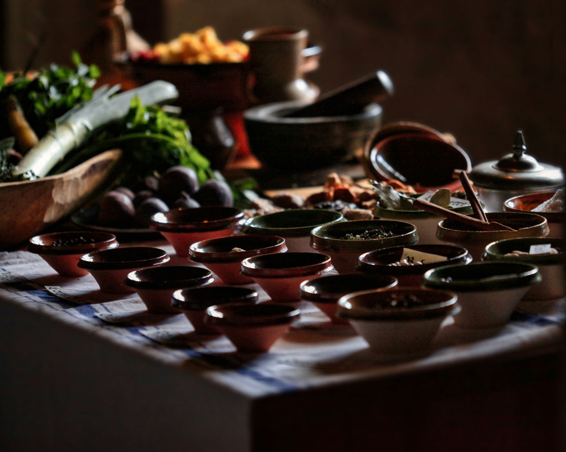 Auf einem rustikalen Küchentisch stehen in sanftem Licht kleine Schüsseln mit Zutaten, frisches Grünzeug sowie ein Mörser mit Stößel.