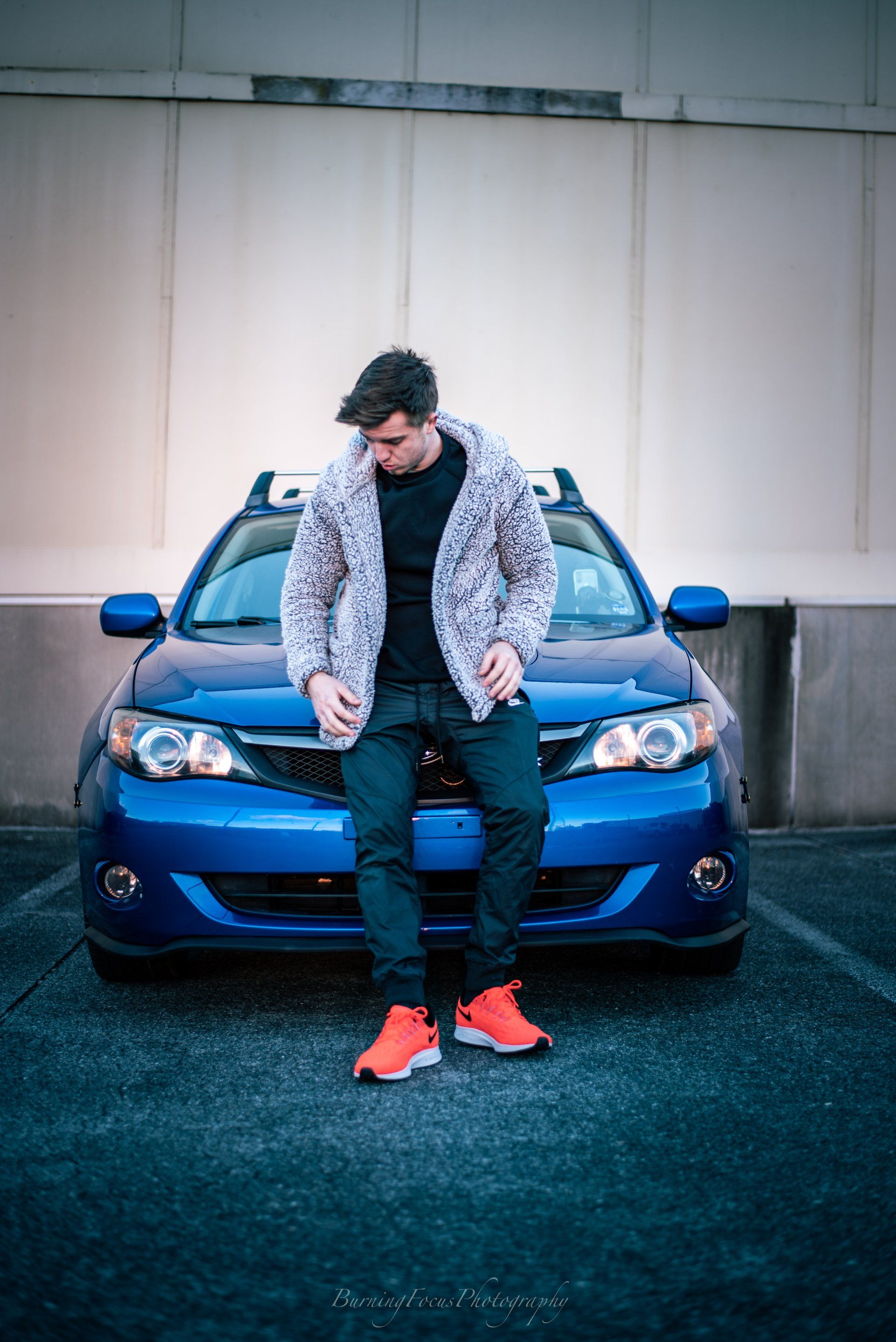 A man is sitting on the front of a blue car.