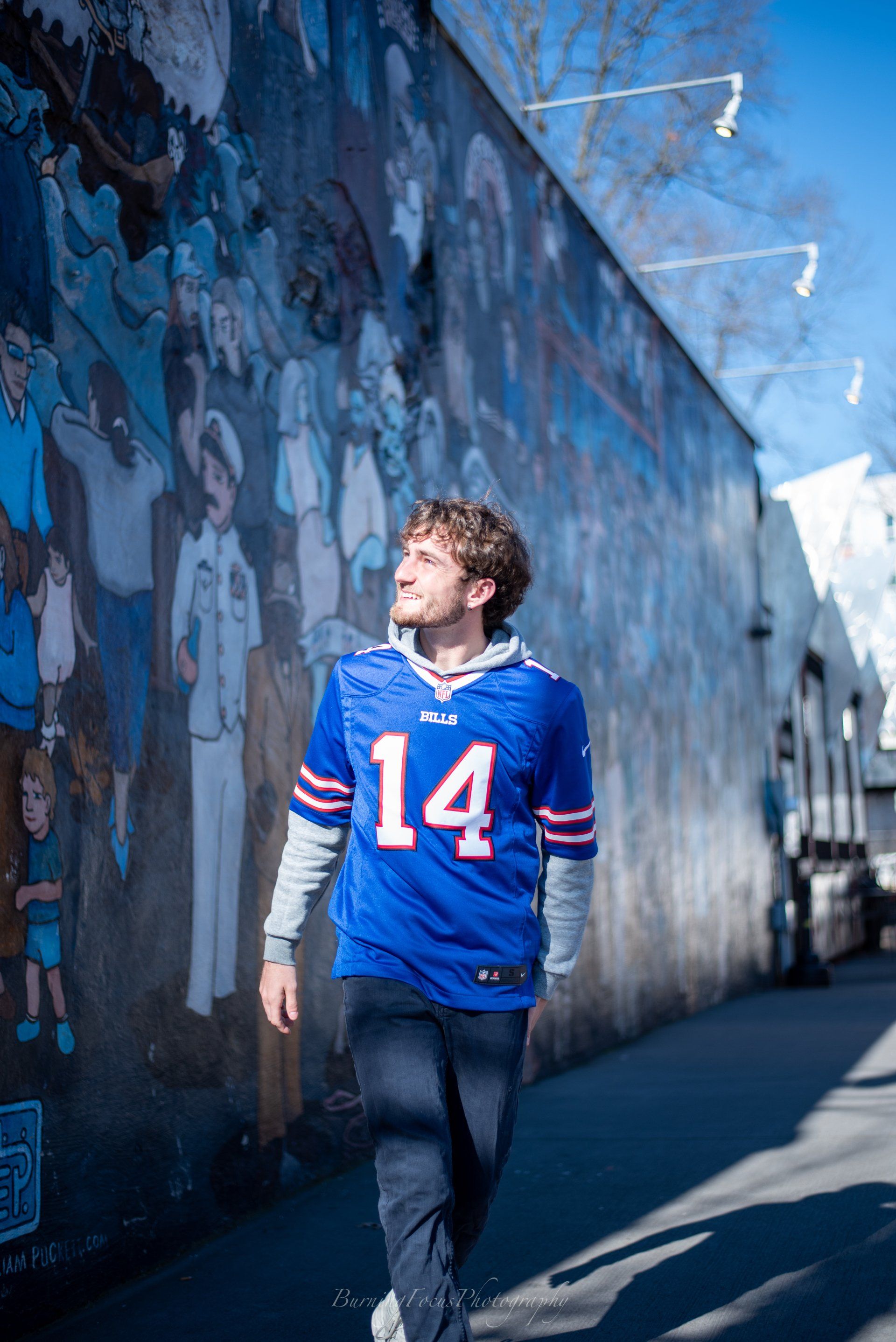A man wearing a buffalo bills jersey is walking down a sidewalk in front of a mural.