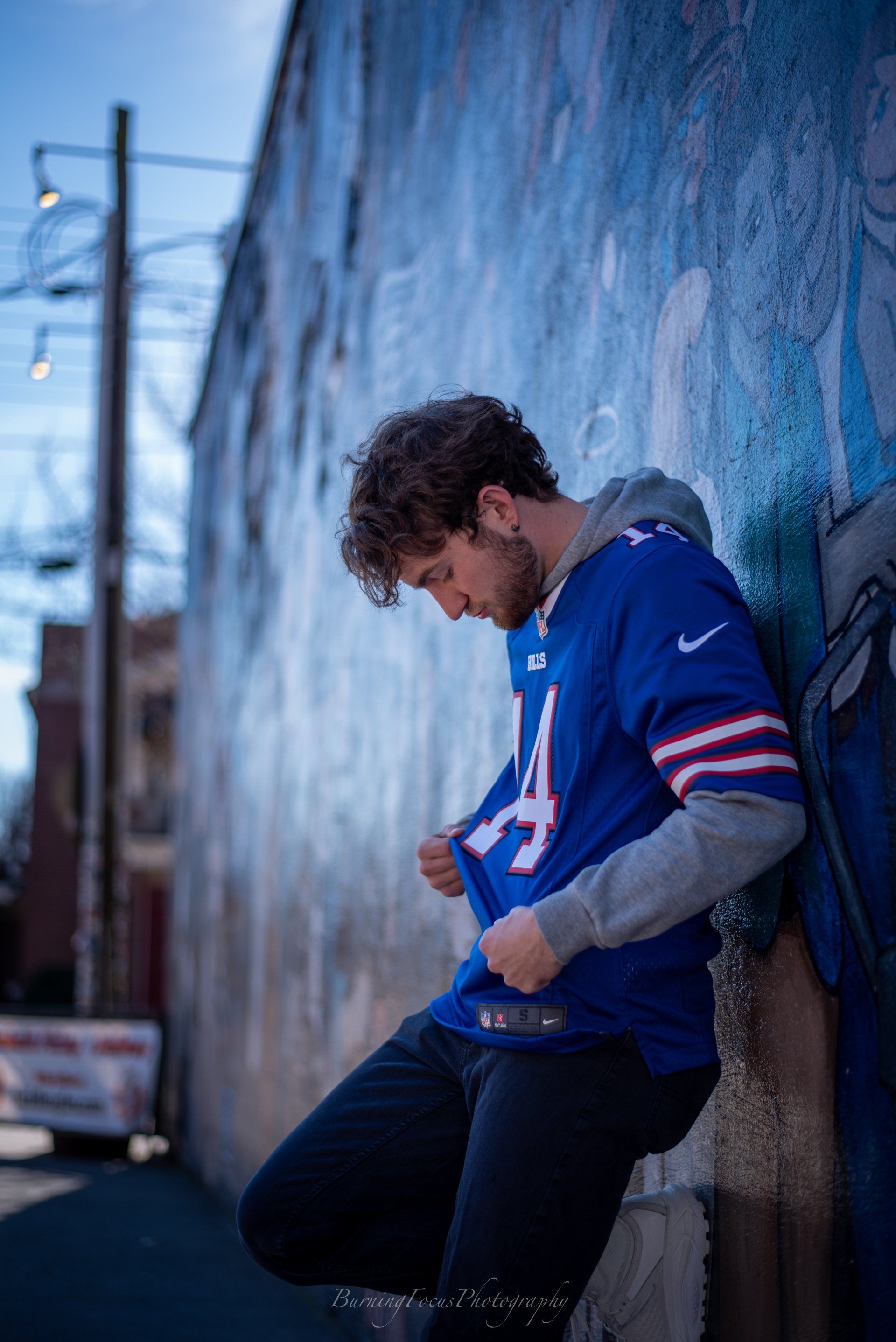 A man in a blue jersey is leaning against a wall.