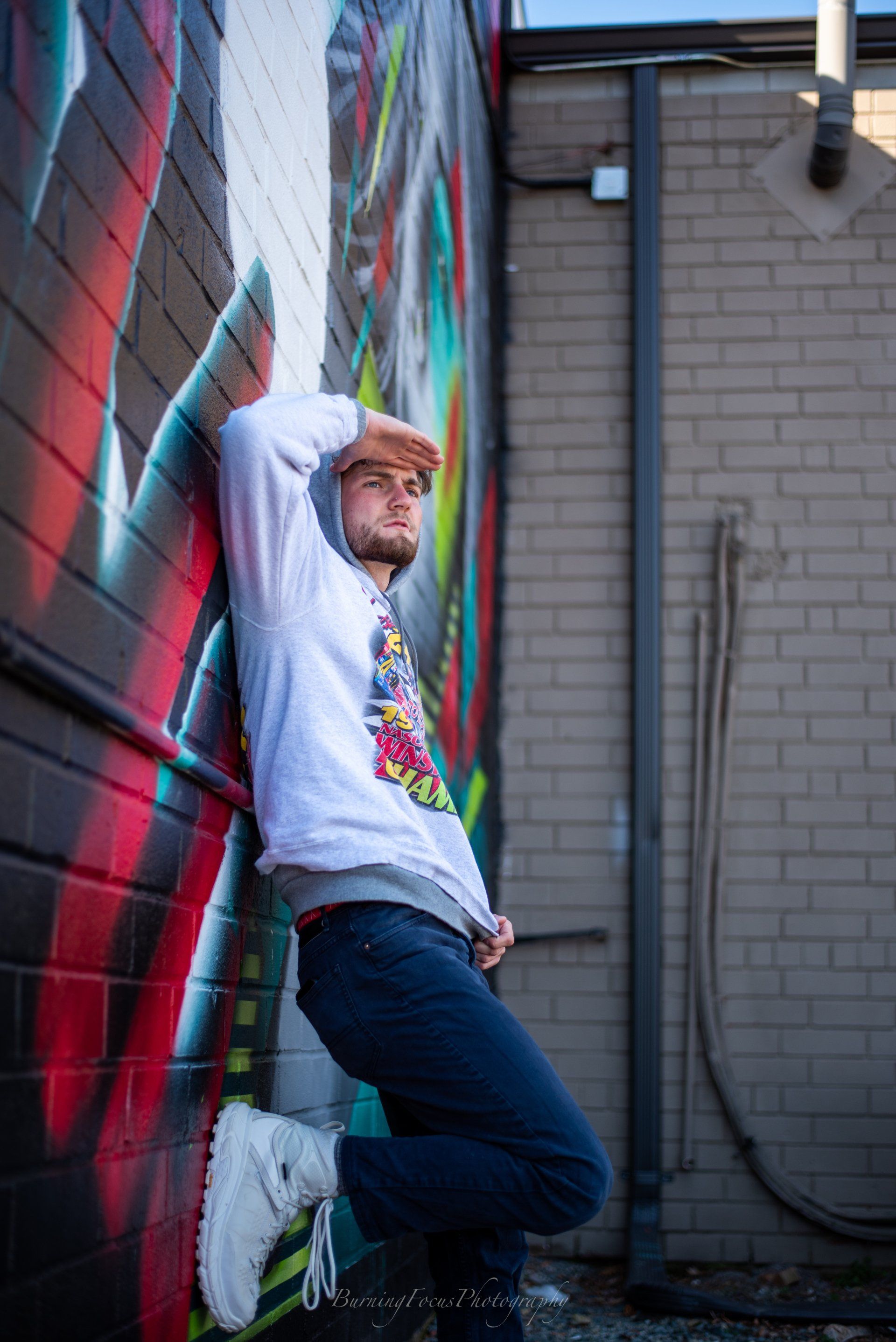 A man is leaning against a brick wall with graffiti on it.