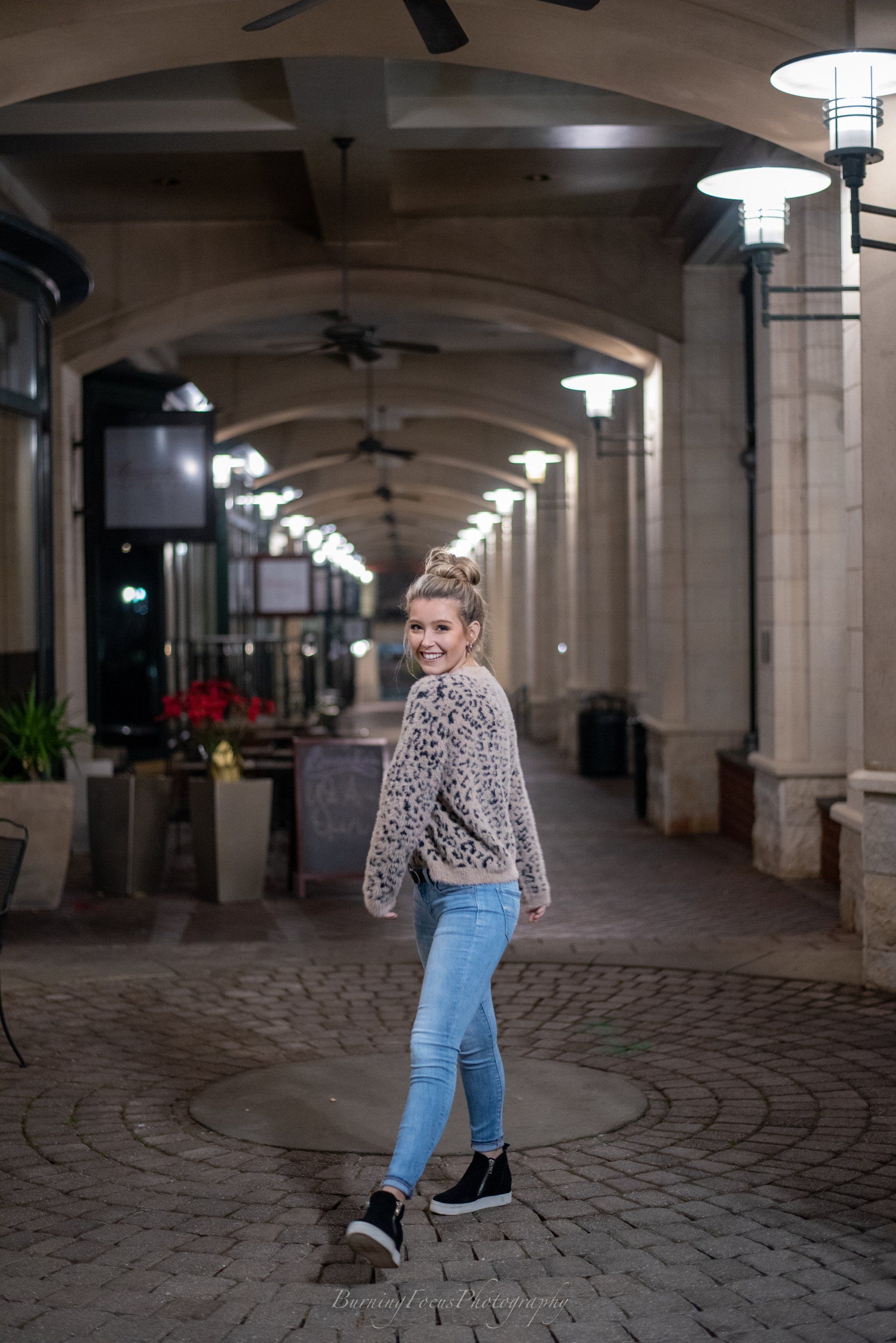 A woman in a sweater and jeans is walking down a cobblestone alleyway.