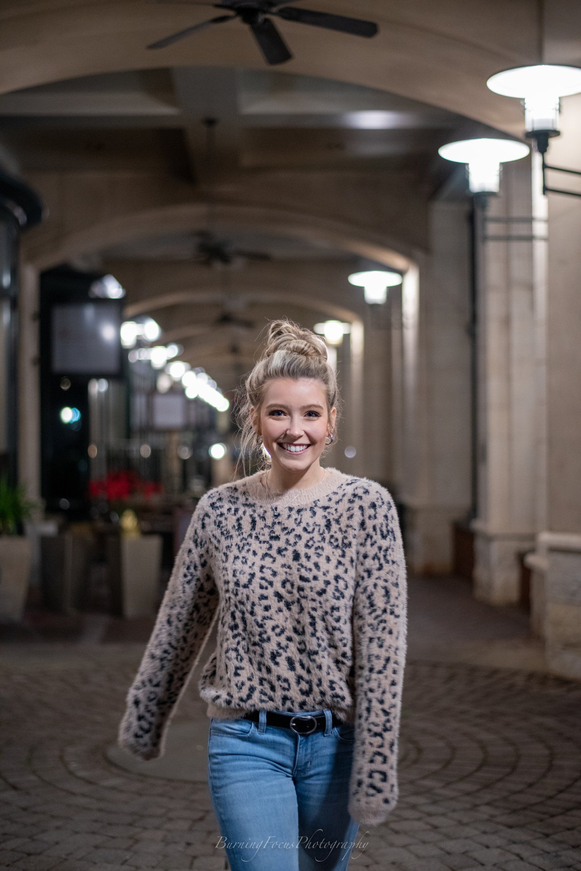 A woman in a leopard print sweater and jeans is walking down a hallway.