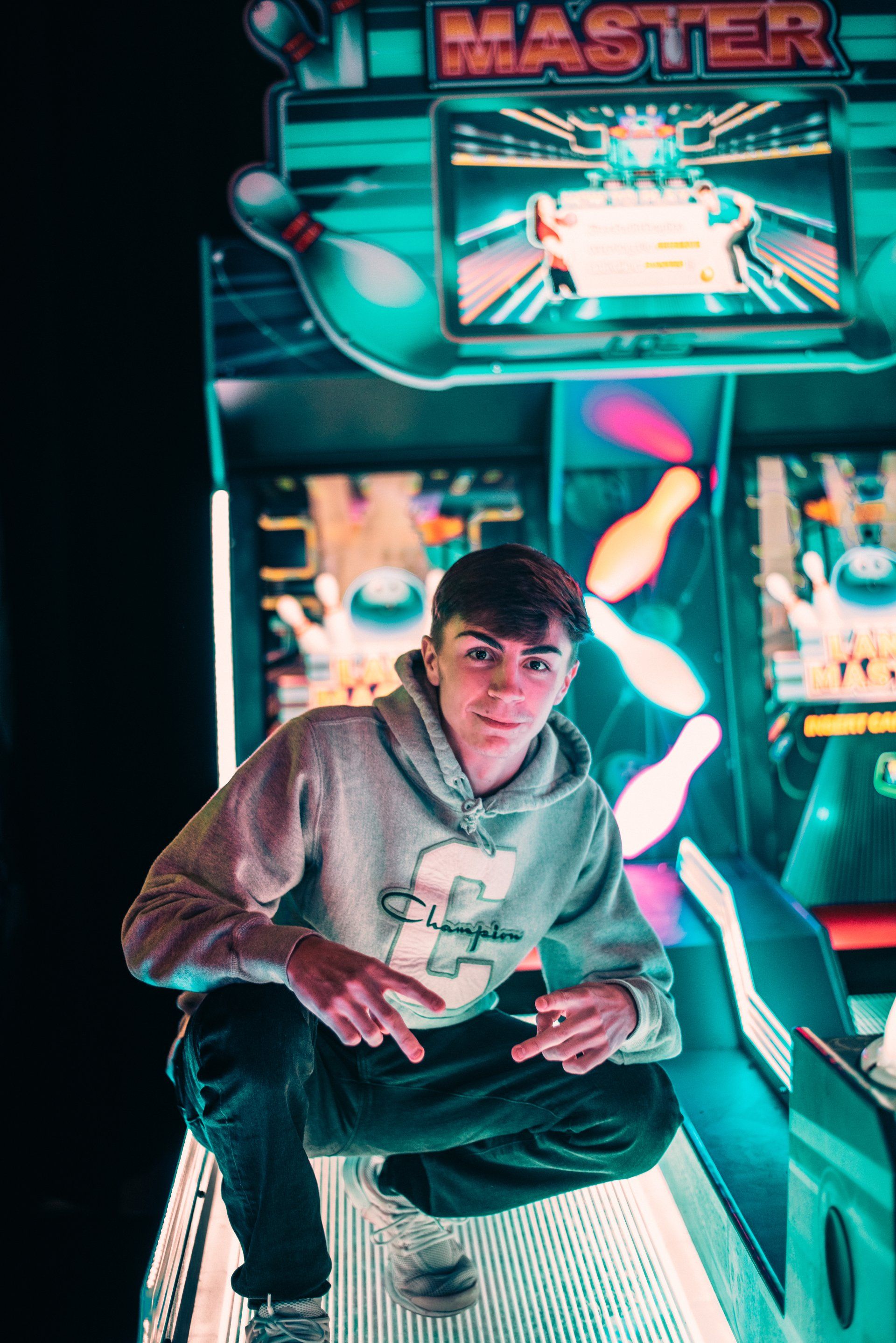 A young man is kneeling down in front of an arcade machine.