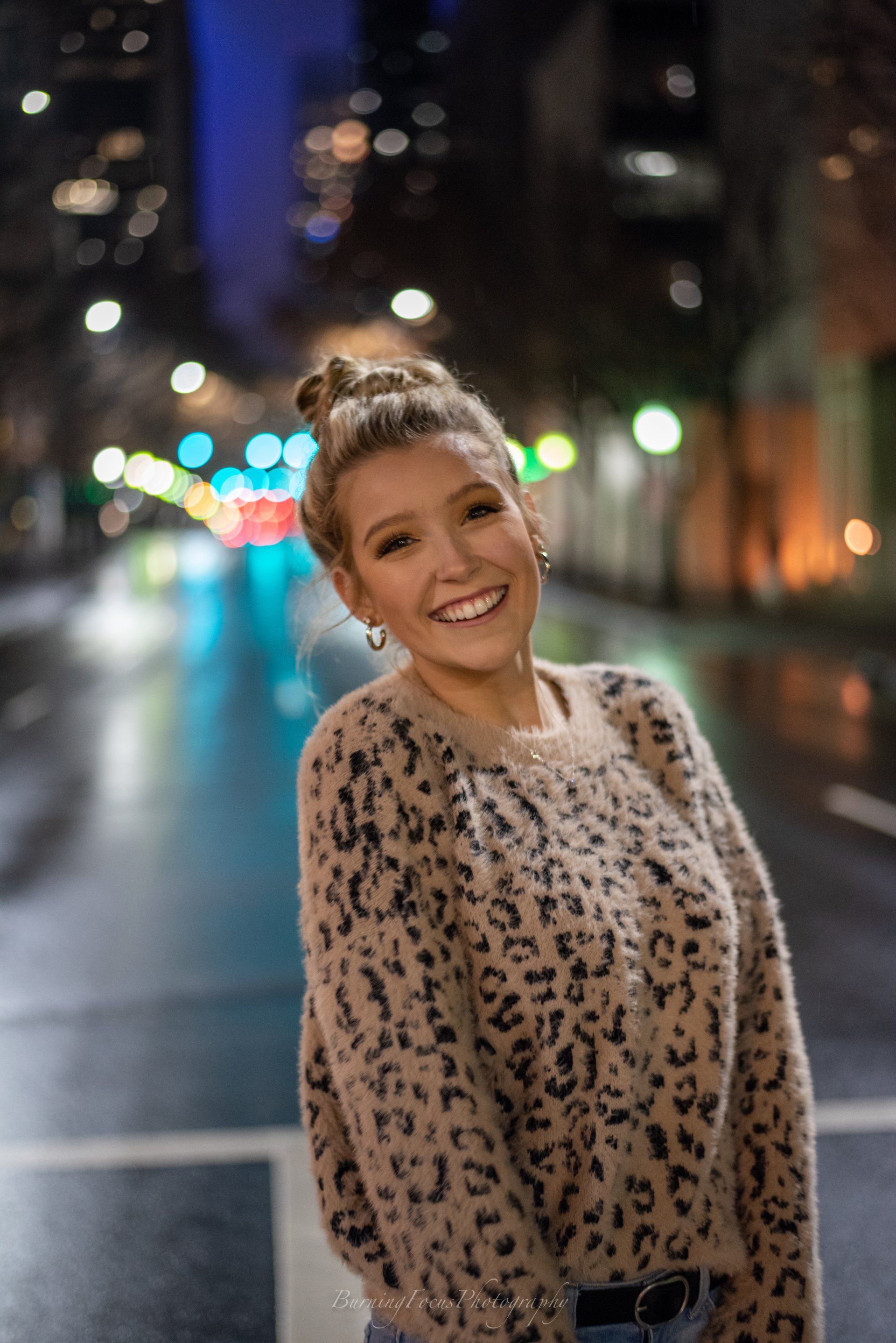 A woman in a leopard print sweater is standing on a city street at night.