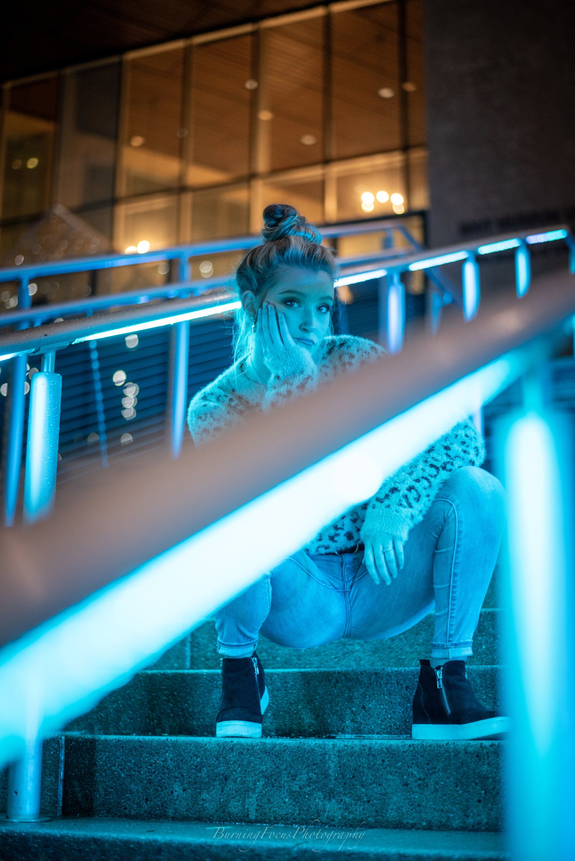 A woman is squatting down on a set of stairs with blue lights behind her.