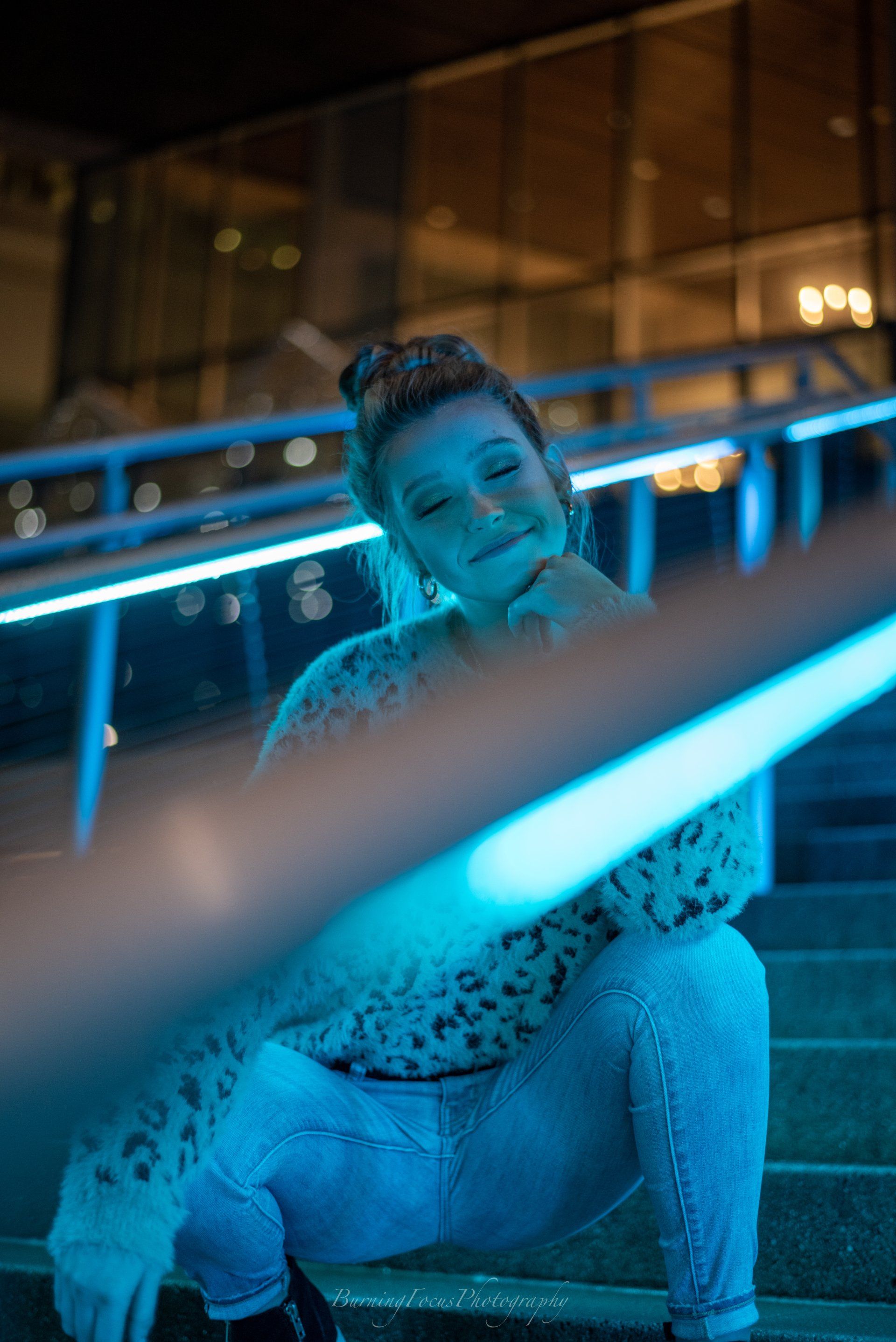 A woman is sitting on a set of stairs with a blue light behind her.