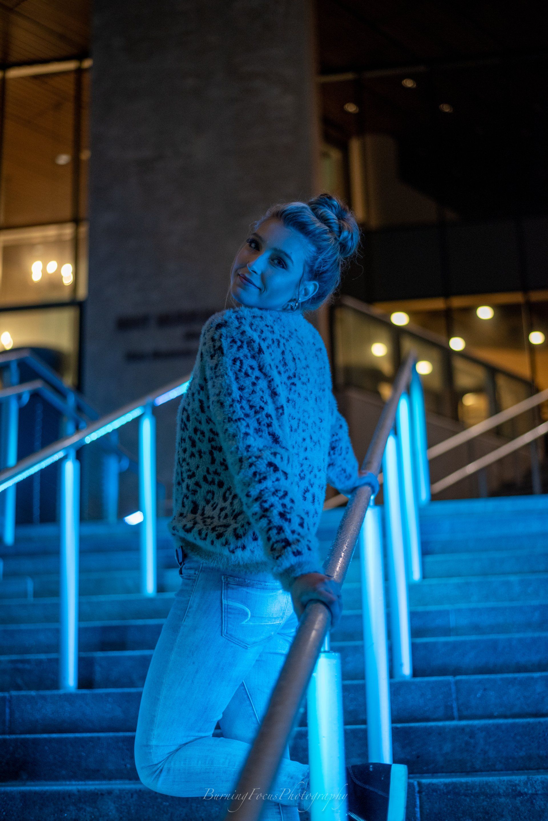 A woman is kneeling down on a set of stairs with blue lights behind her.