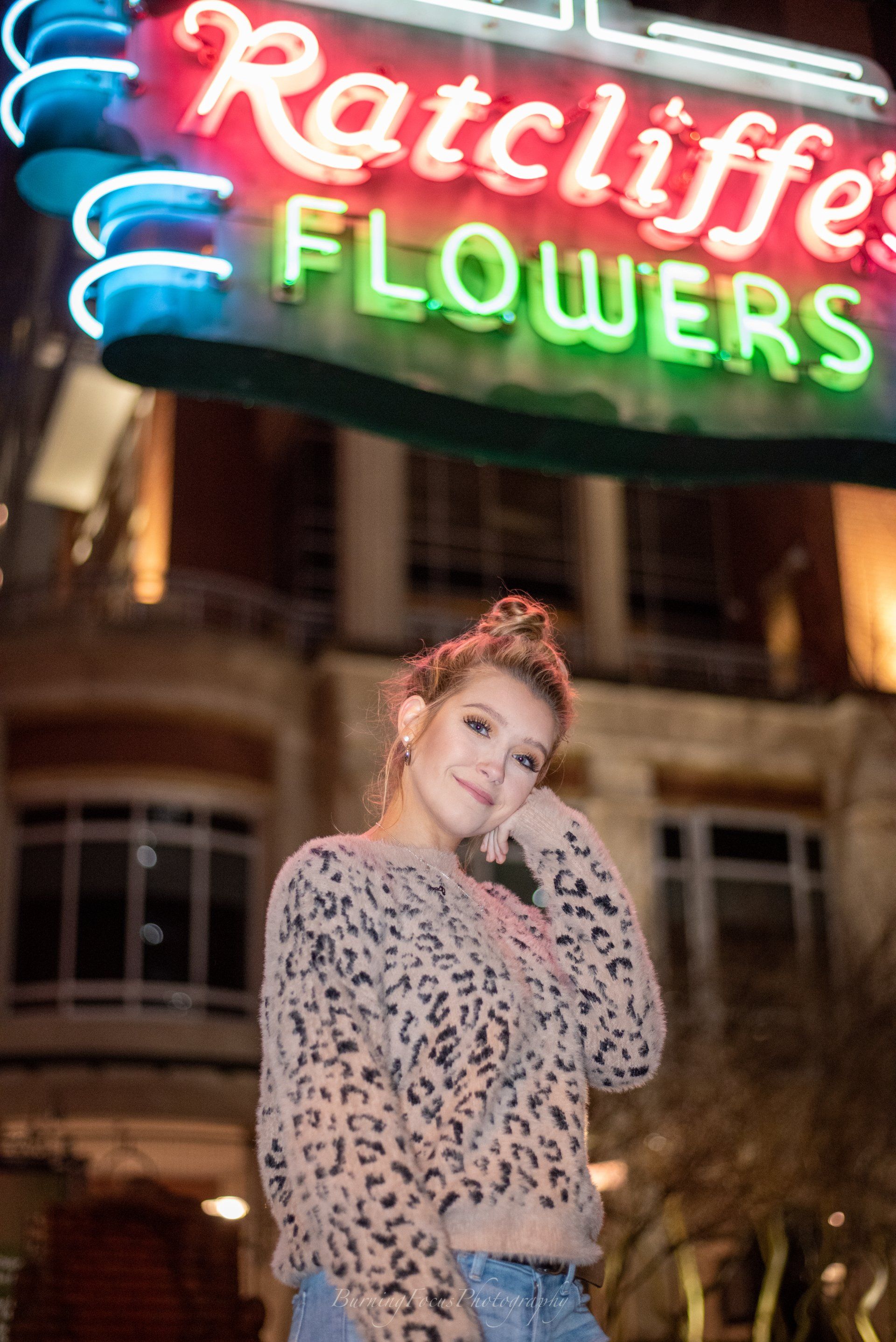A woman is standing in front of a neon sign for ratcliffe flowers.