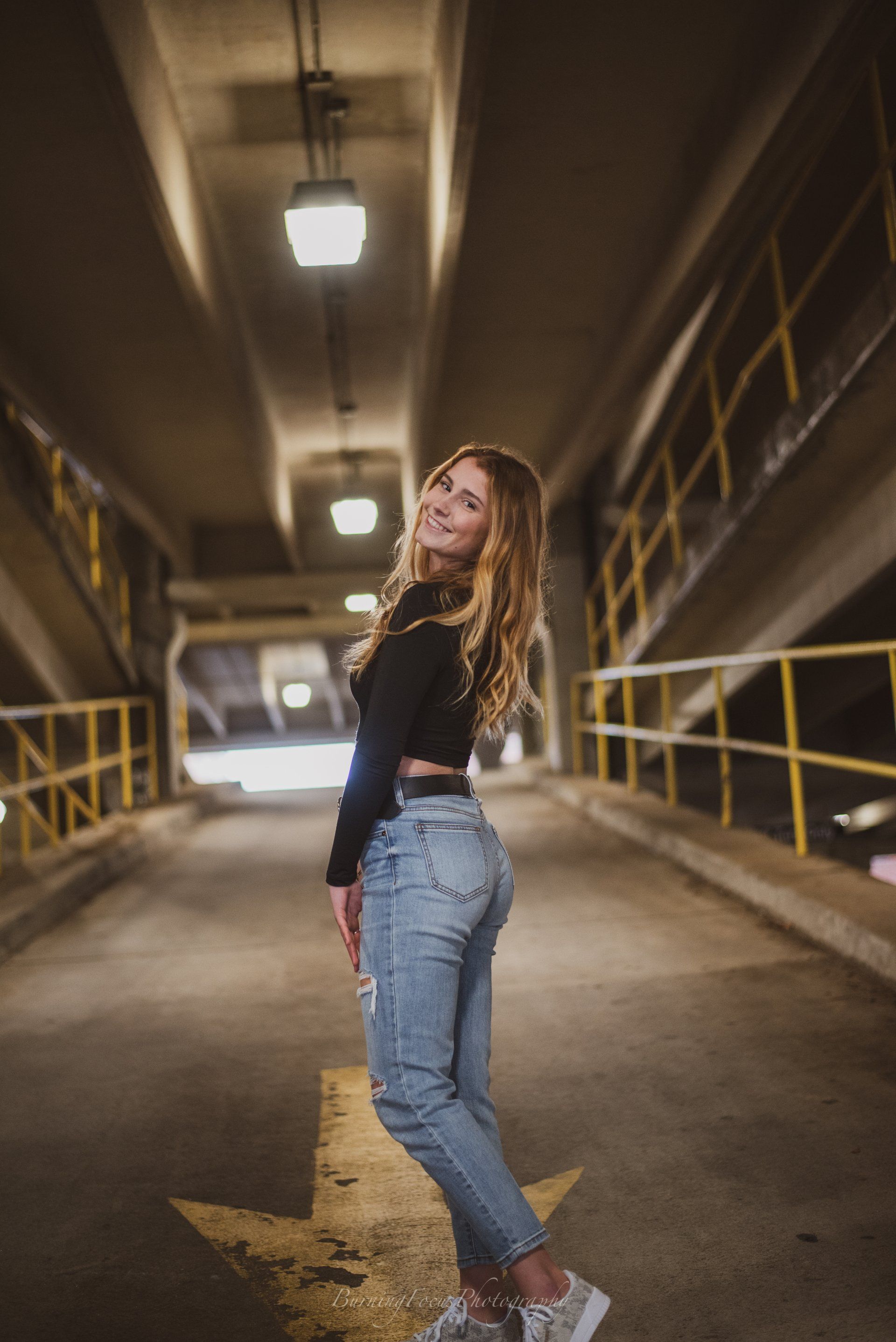 A woman in a black crop top and jeans is standing in a parking garage.