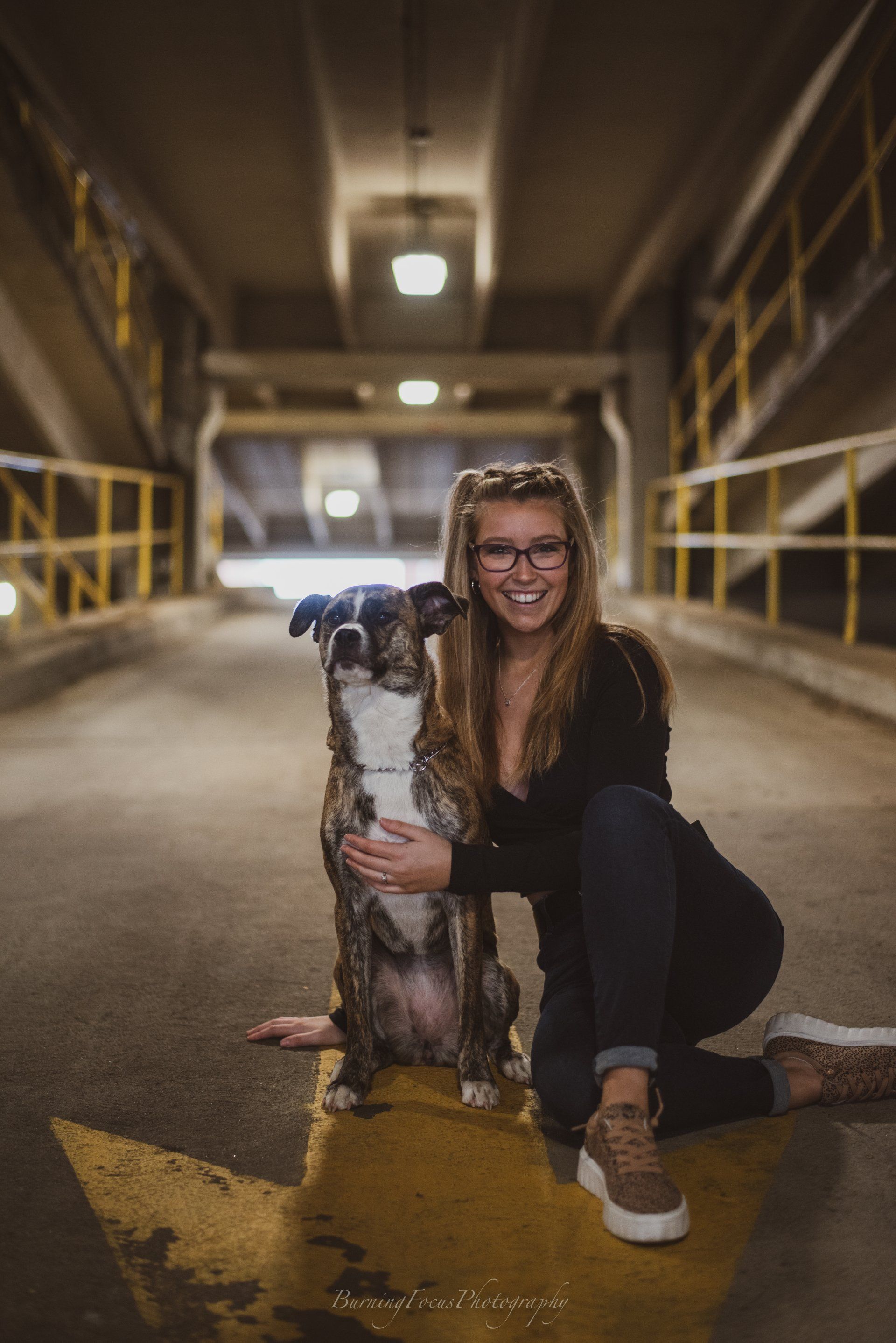 A woman is kneeling down with her dog in a parking garage.