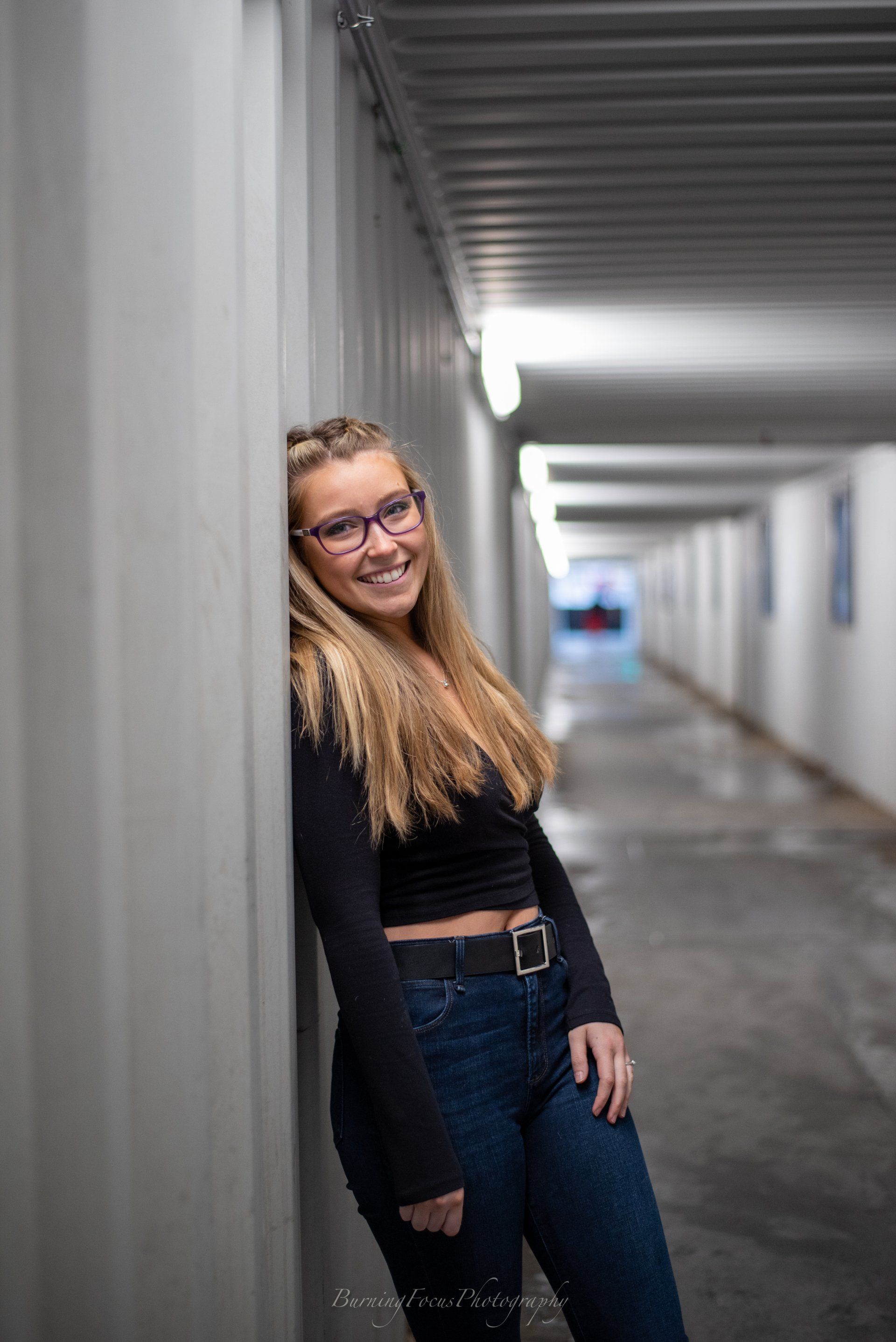 A young woman wearing glasses is leaning against a wall in a tunnel.