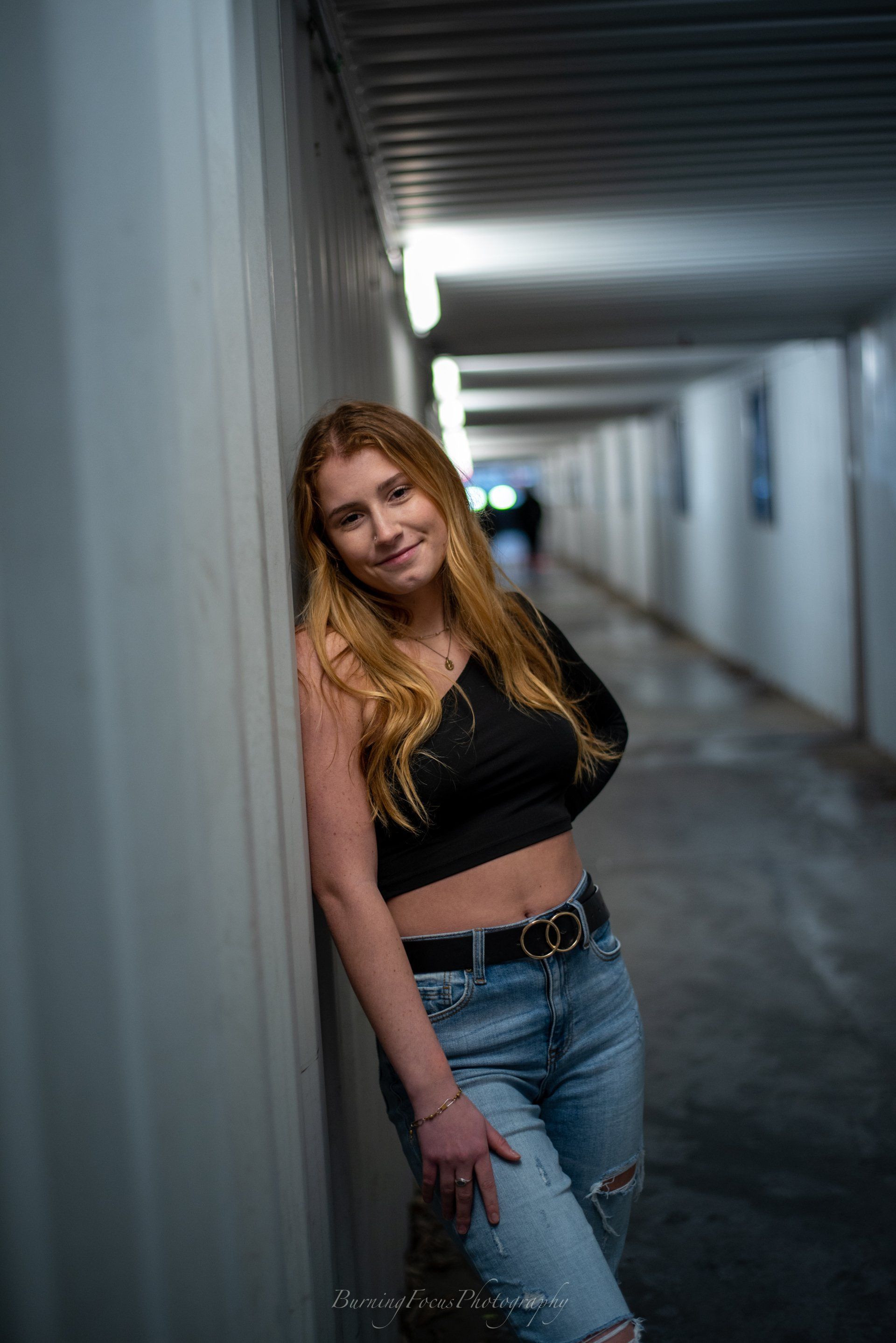 A woman is leaning against a wall in a hallway.