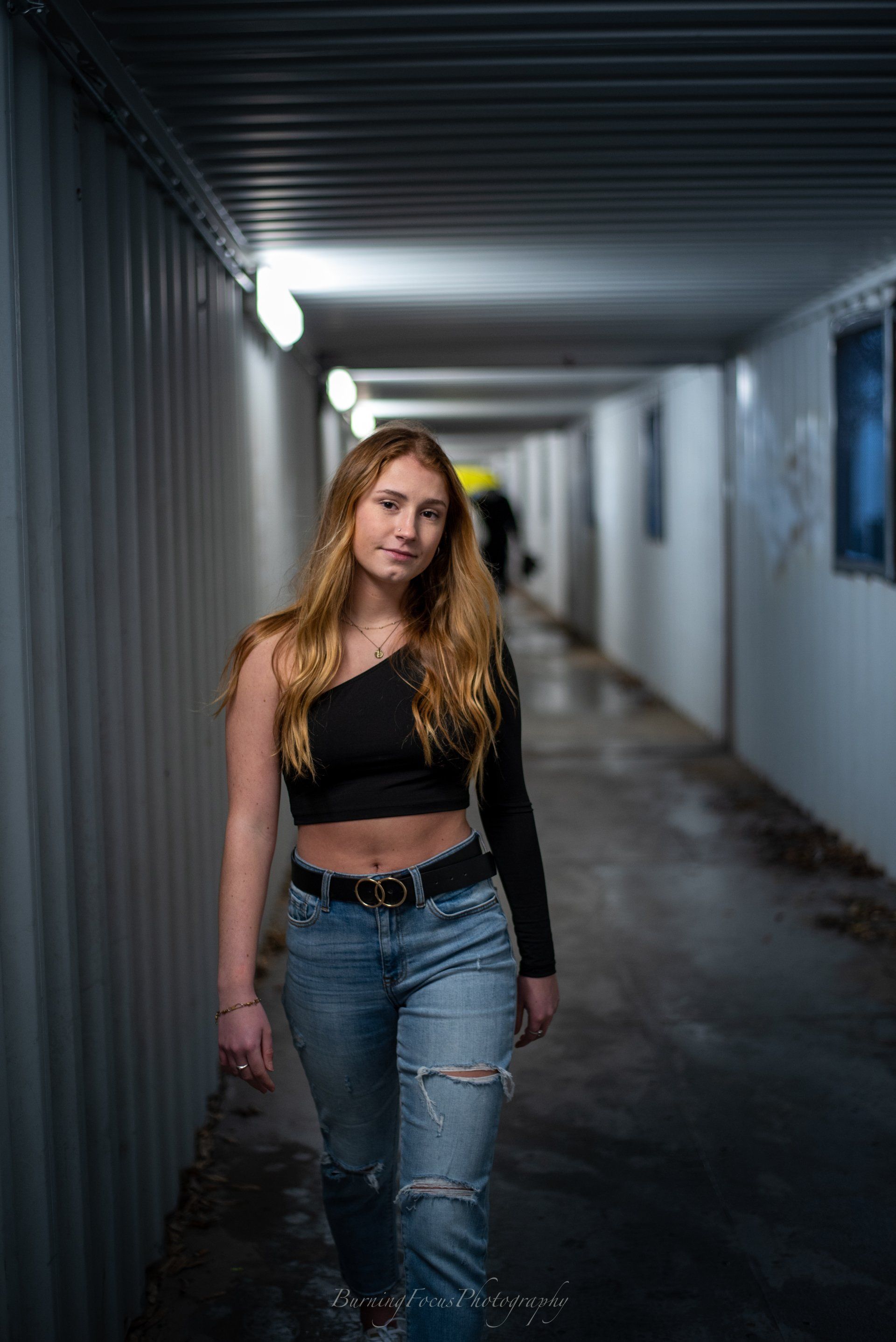 A young woman is standing in a tunnel wearing a black crop top and jeans.
