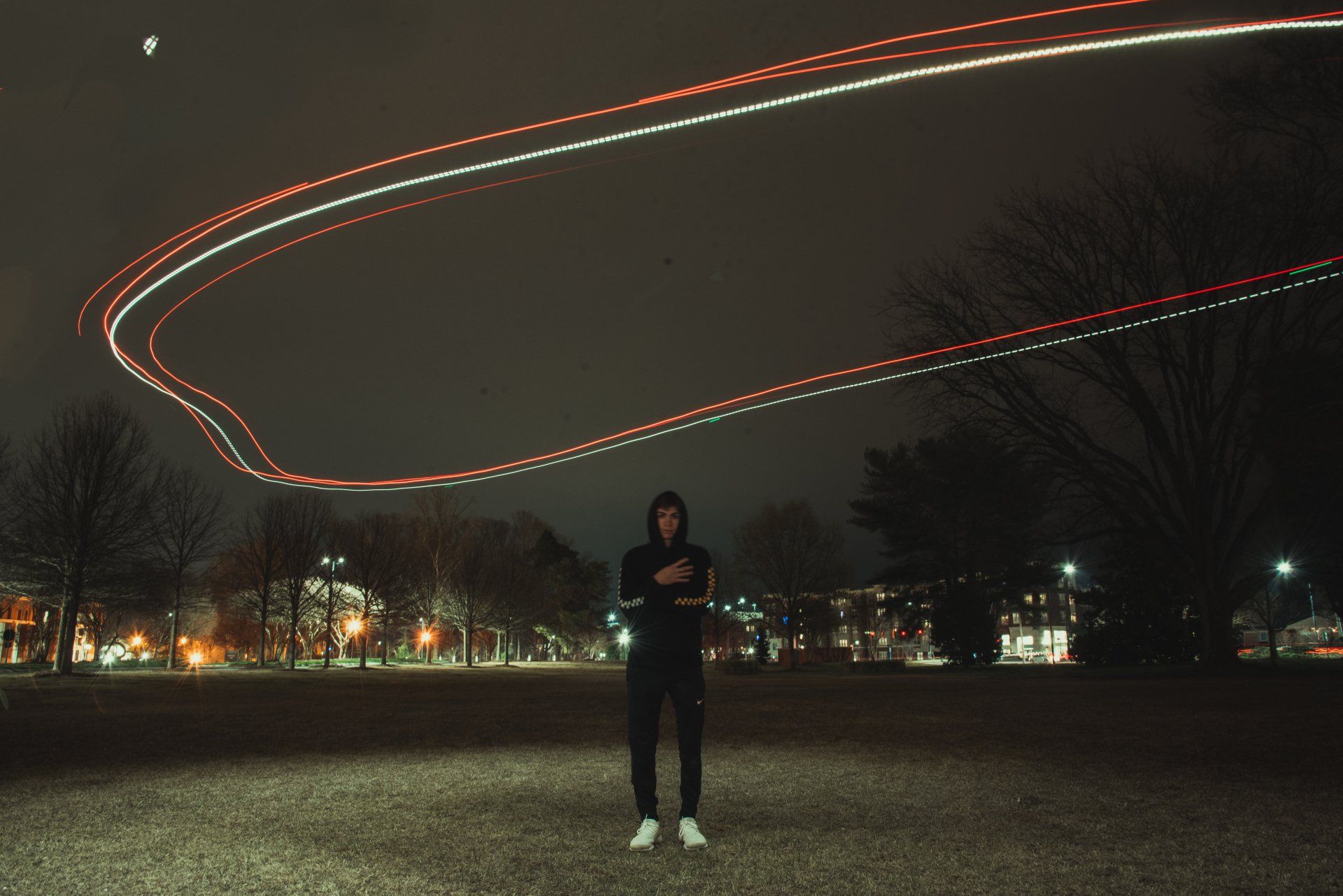 A man in a hoodie is standing in a field at night.