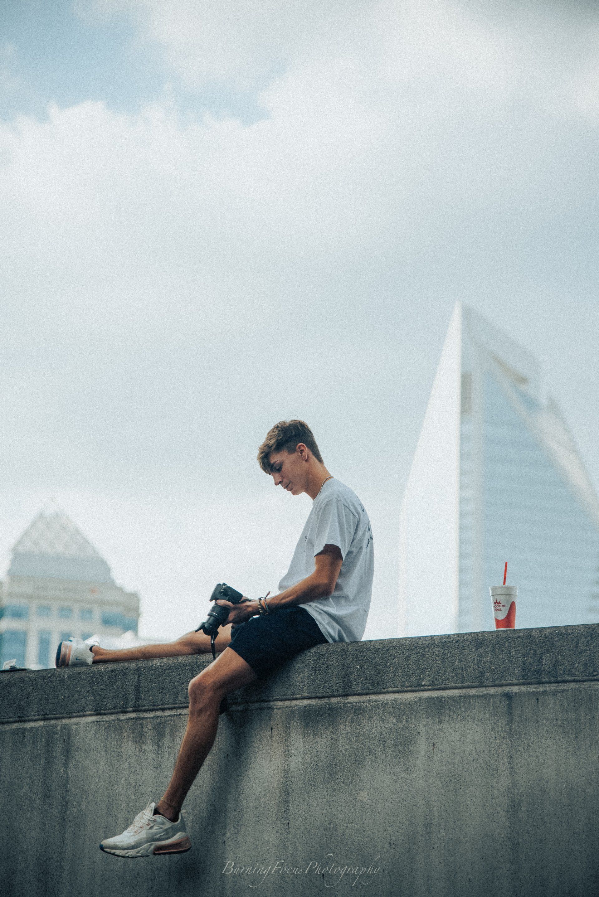 A young man is sitting on a wall with his legs crossed.