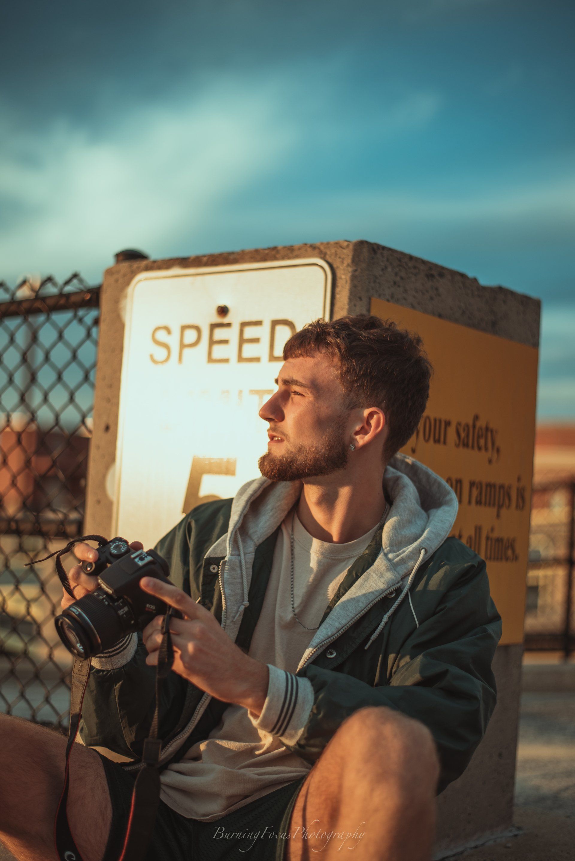 A man is sitting on the ground holding a camera in front of a speed limit sign.