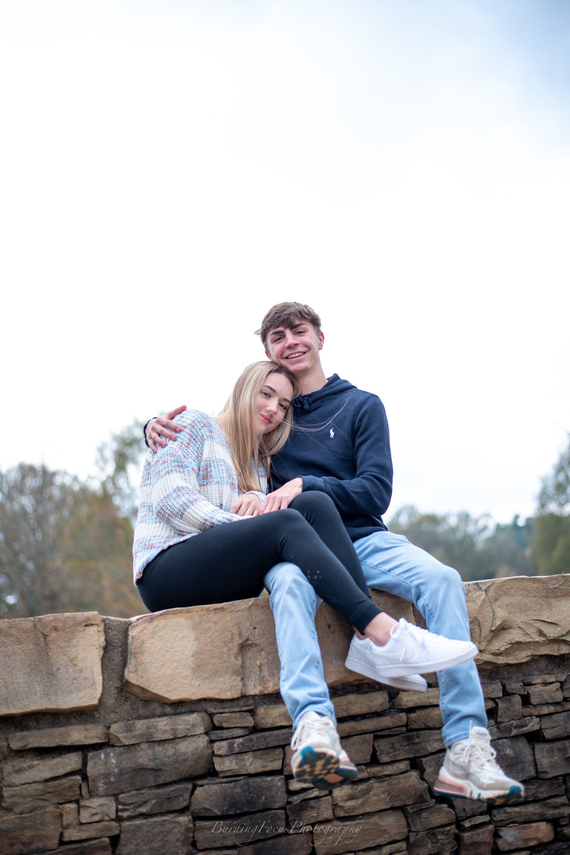 A man and a woman are sitting on a stone wall.