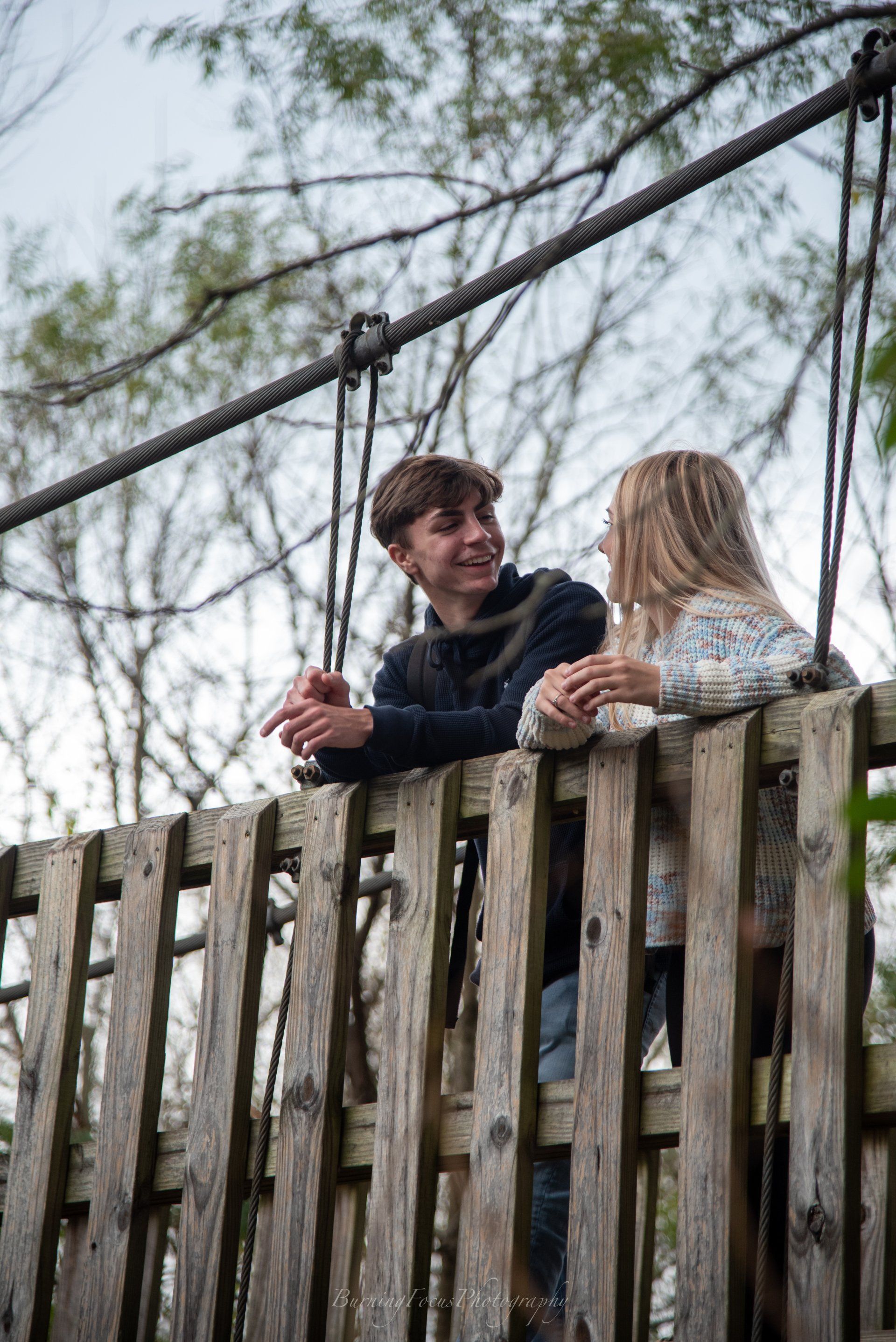 A boy and a girl are sitting on top of a wooden fence.