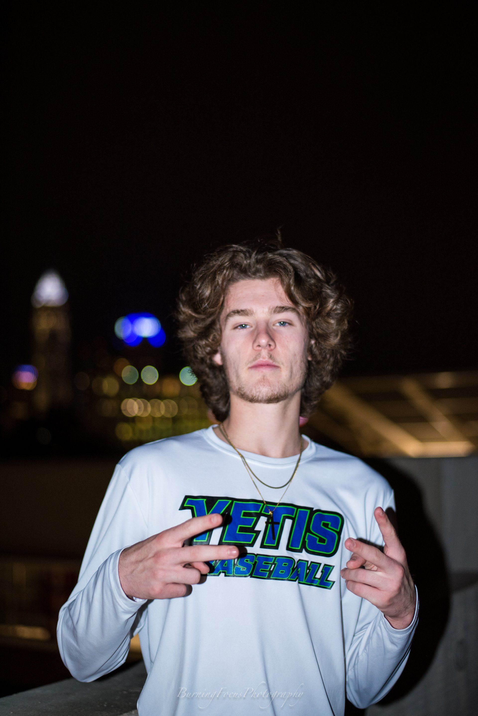 A young man wearing a white sweatshirt is standing on a balcony at night.