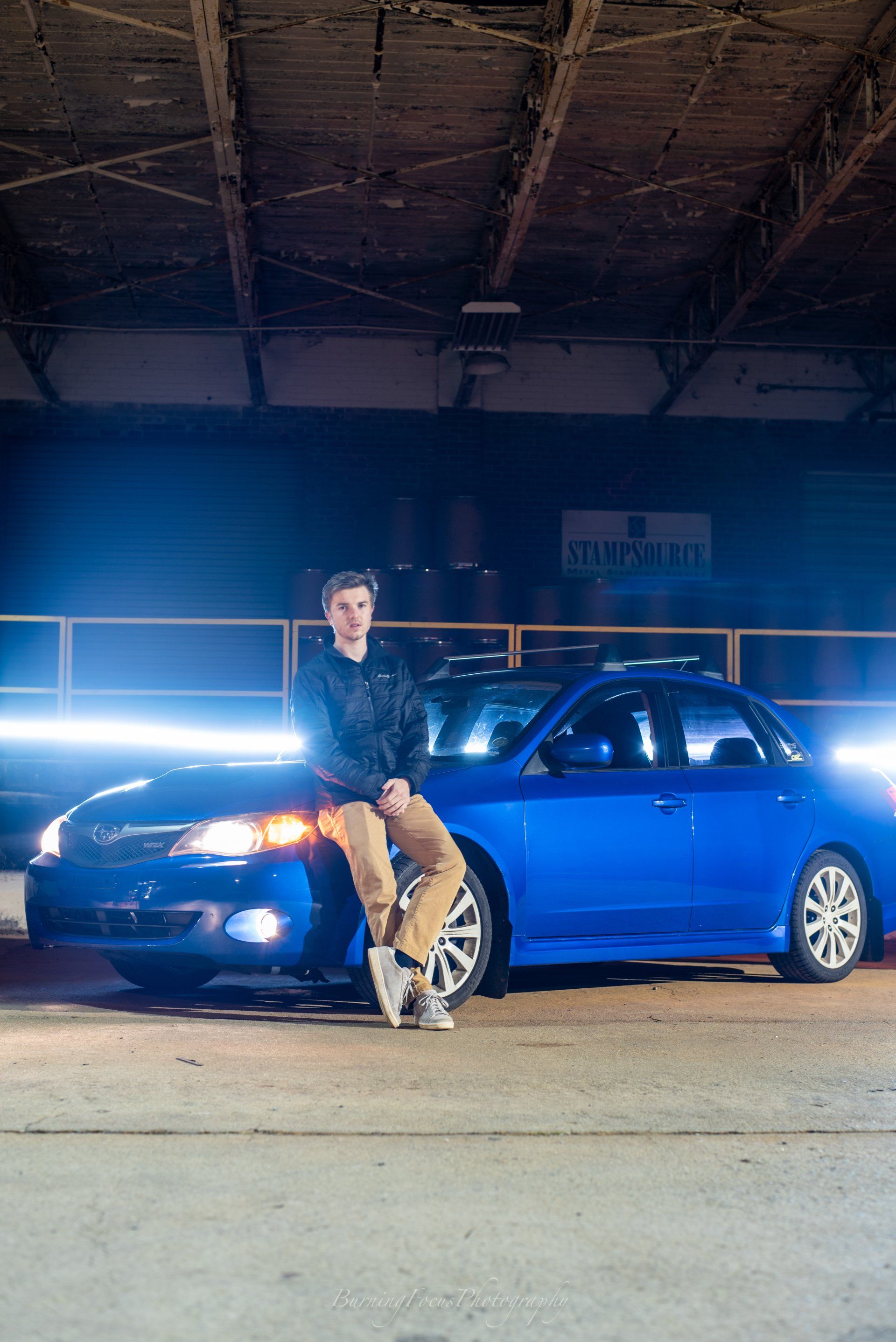 A man is standing next to a blue car in a garage.