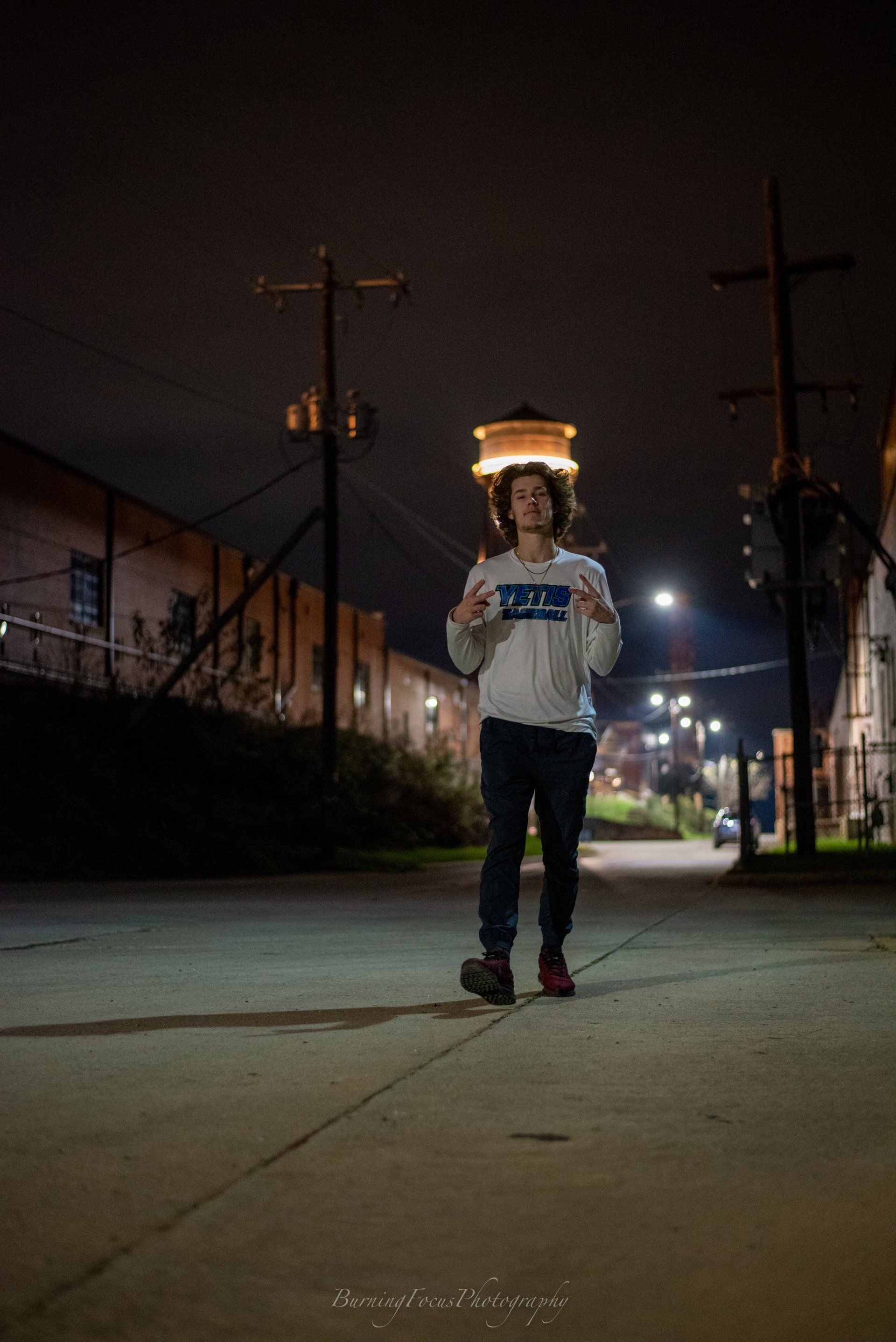 A young man is walking down a sidewalk at night.