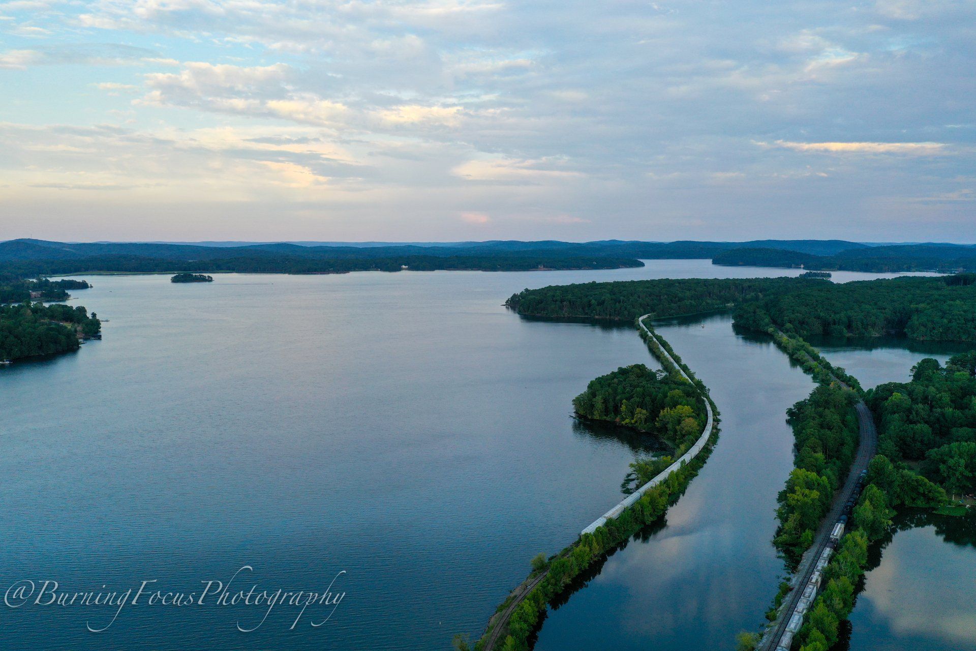 An aerial view of a large body of water surrounded by trees and a road.
