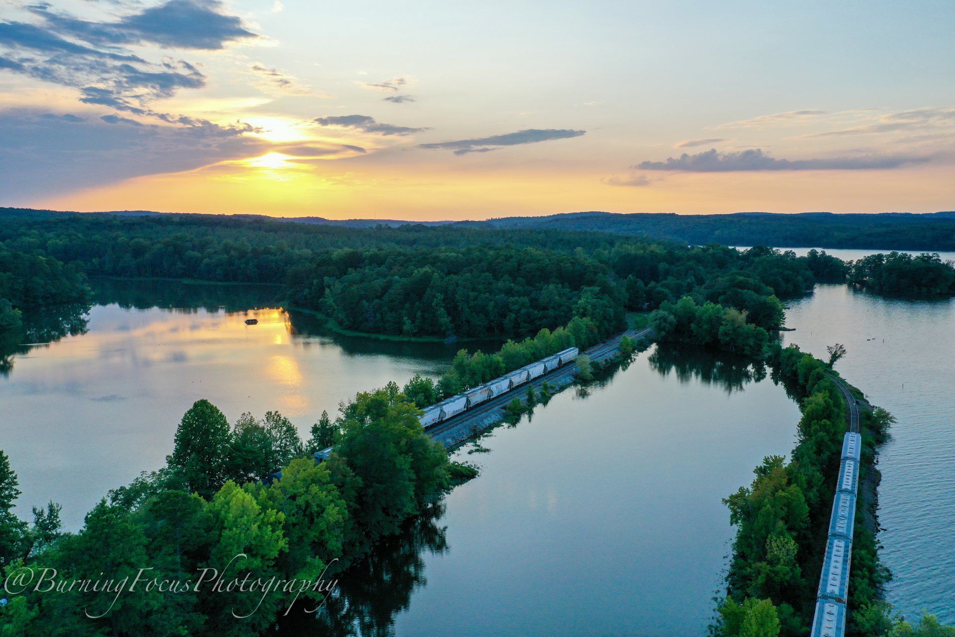 An aerial view of a lake with a train going over it at sunset.
