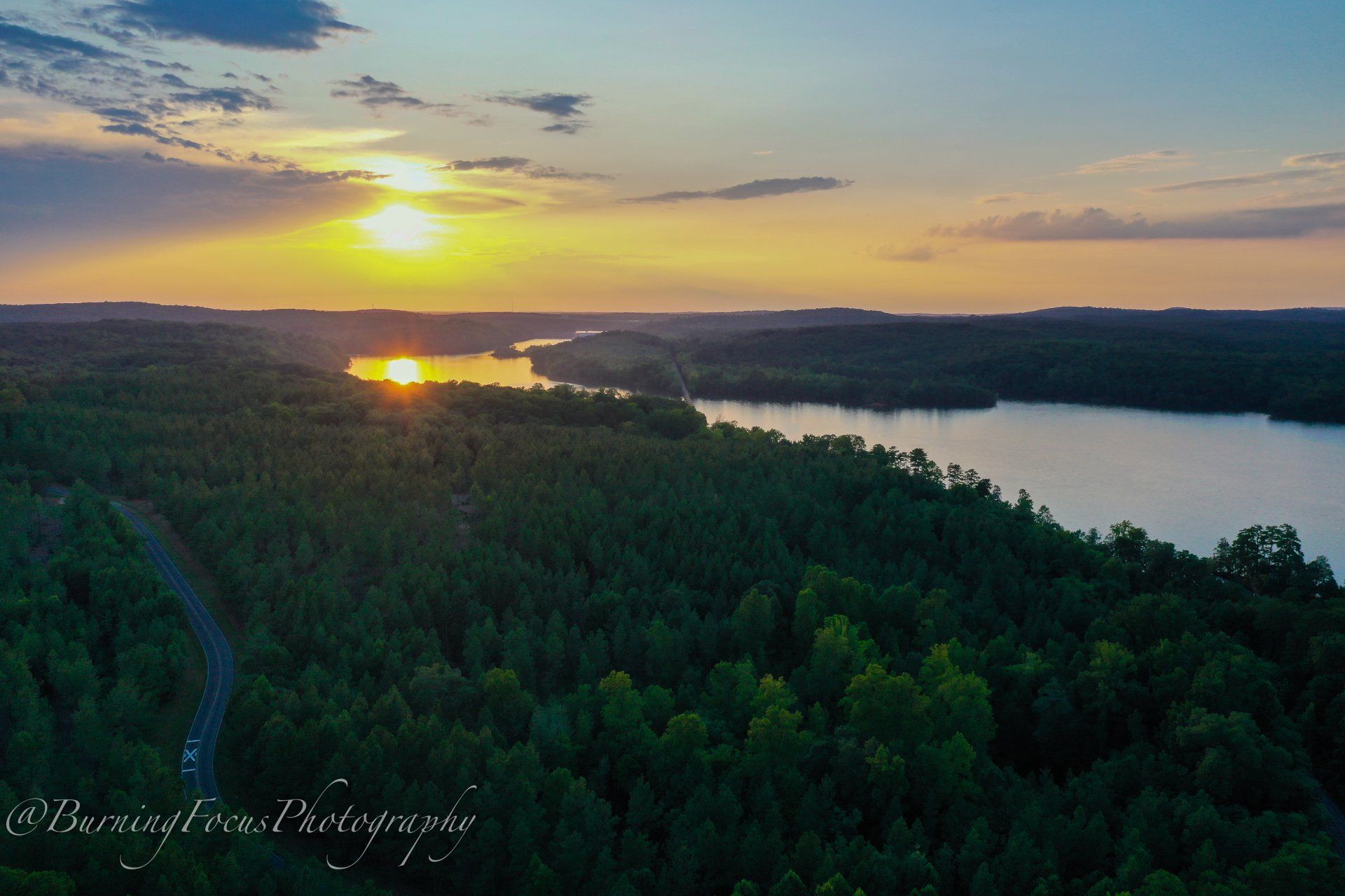 An aerial view of a lake surrounded by trees at sunset.