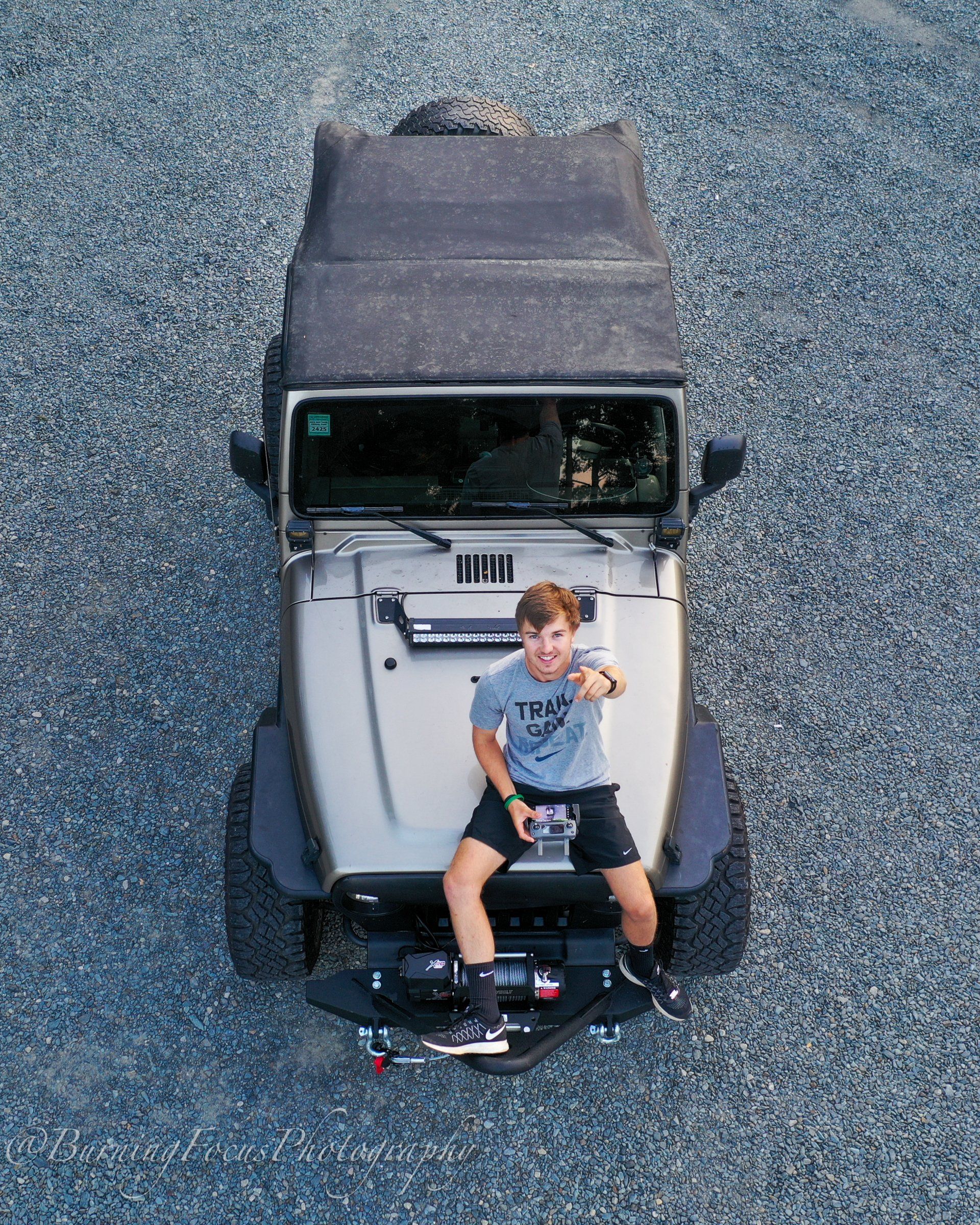 A young man is sitting on the hood of a jeep.