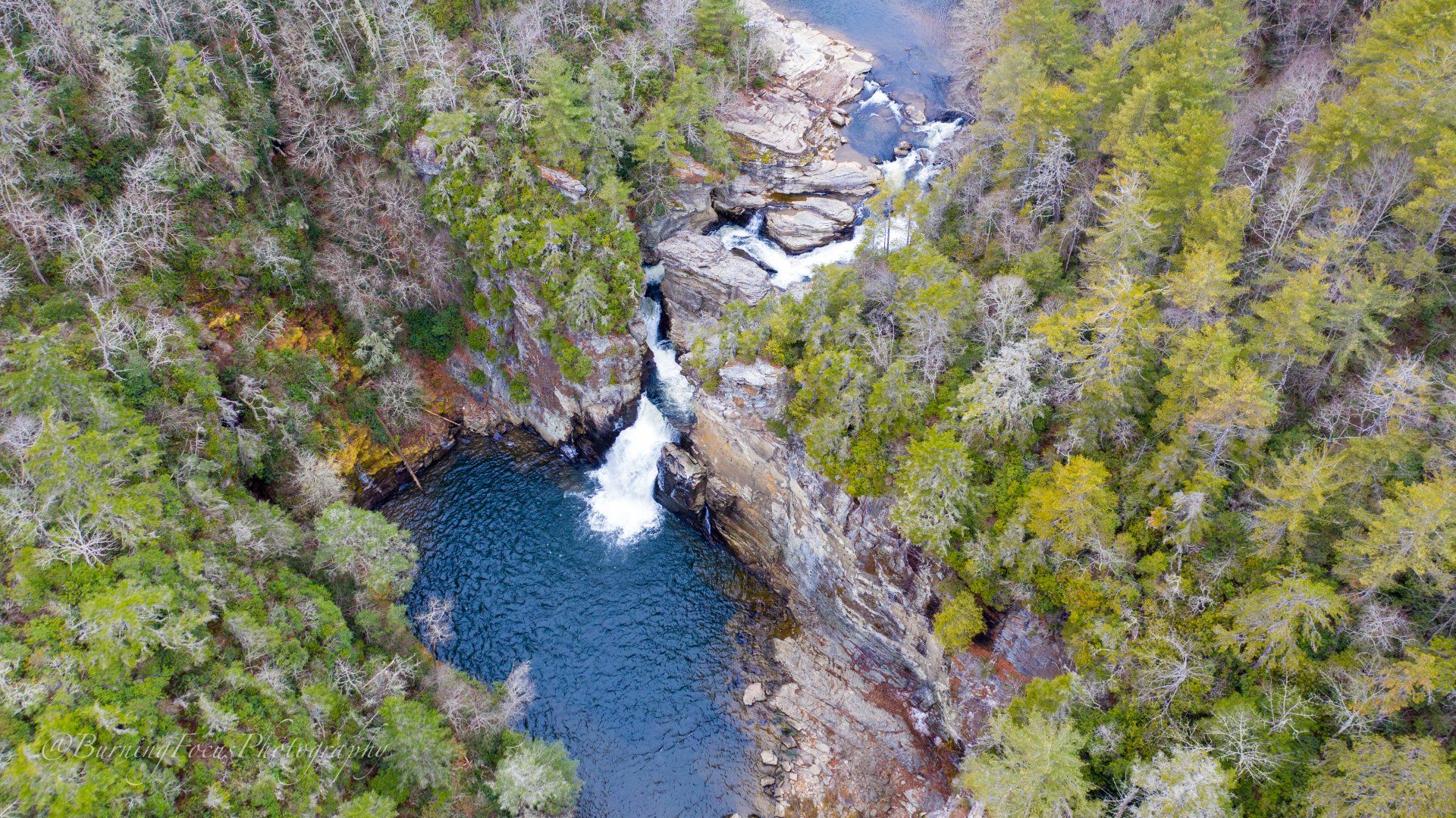An aerial view of a waterfall in the middle of a forest surrounded by trees.