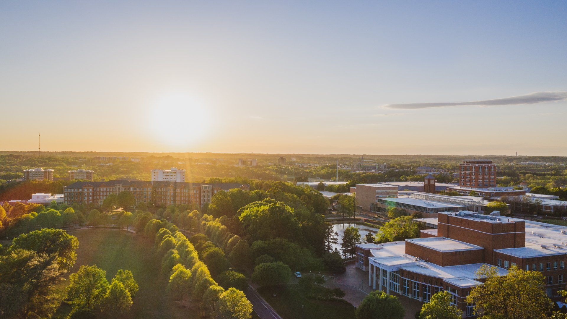 An aerial view of a city at sunset with buildings and trees in the foreground.