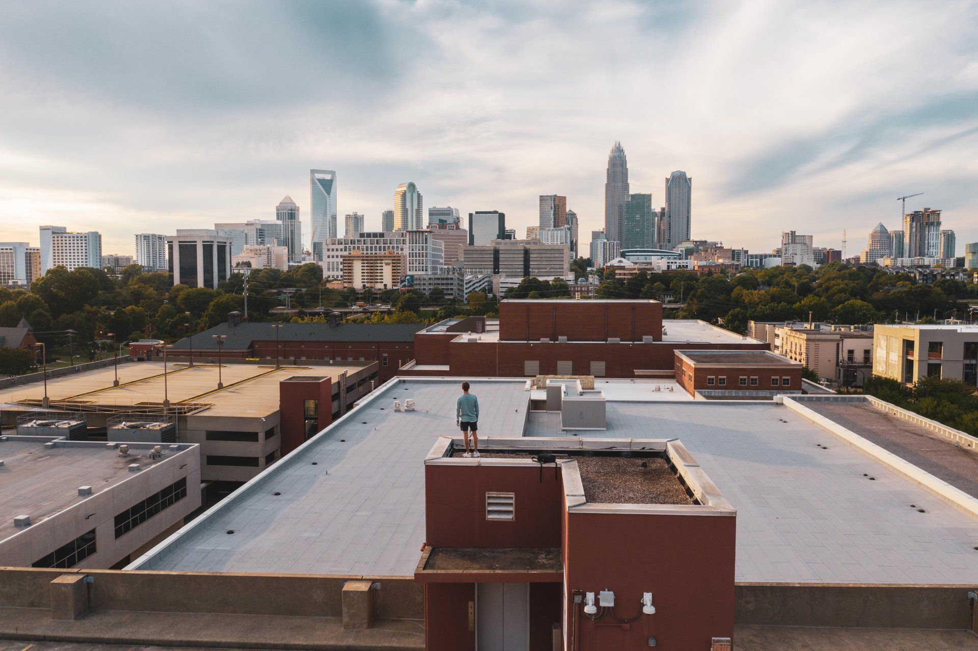 A man is standing on the roof of a building with a city skyline in the background.